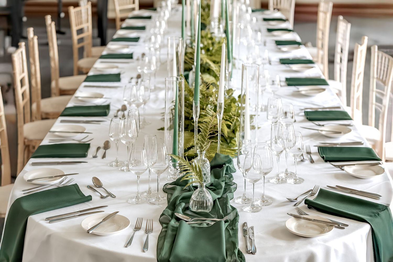 An elegant table setting with green napkins, white linens, wine glasses and floral centerpieces for a formal dining event.