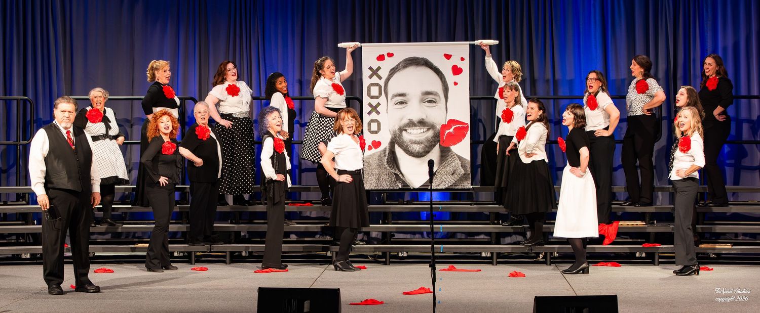 Group of performers on stage in black and red outfits beside a large XOXO banner at a Valentine's Day show.