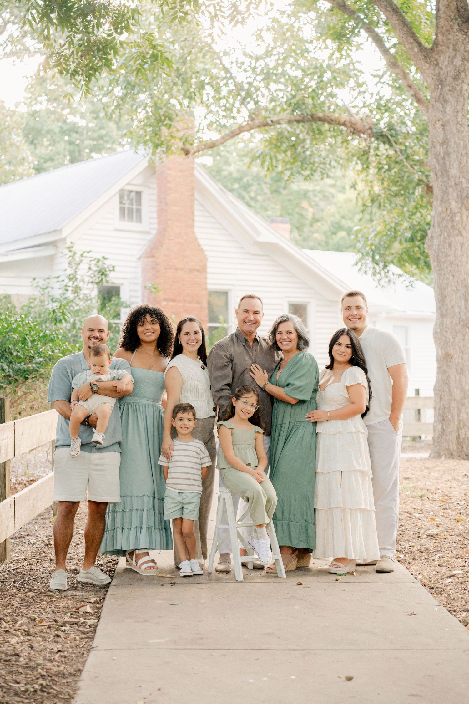 A group in coordinating sage green and white outfits poses together outdoors on a path surrounded by trees.