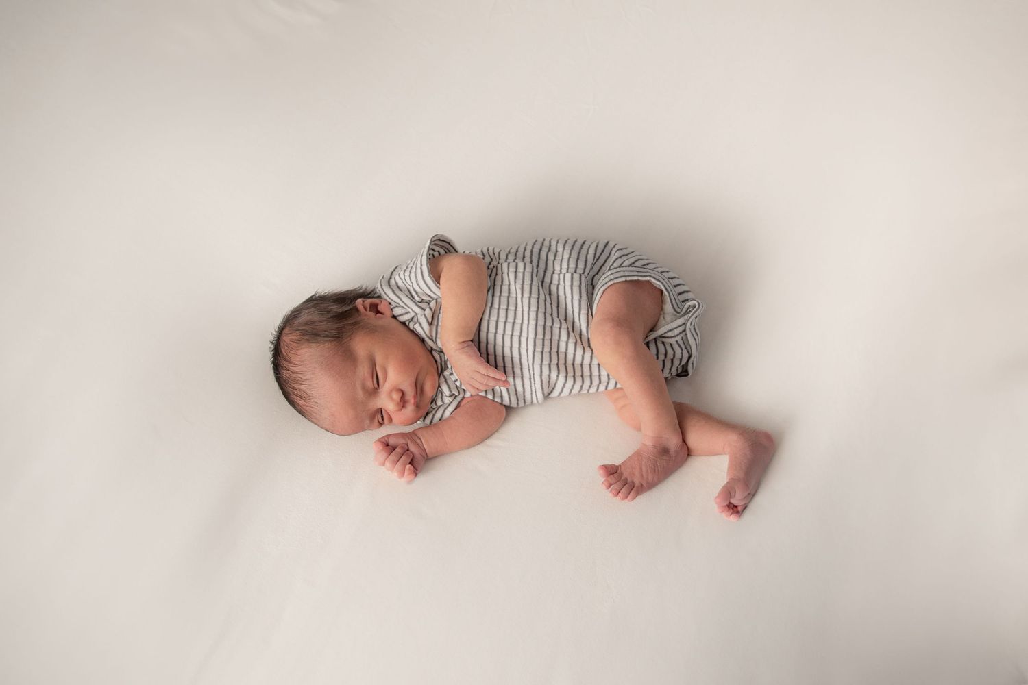 Sleeping baby wearing striped onesie lying on white background.