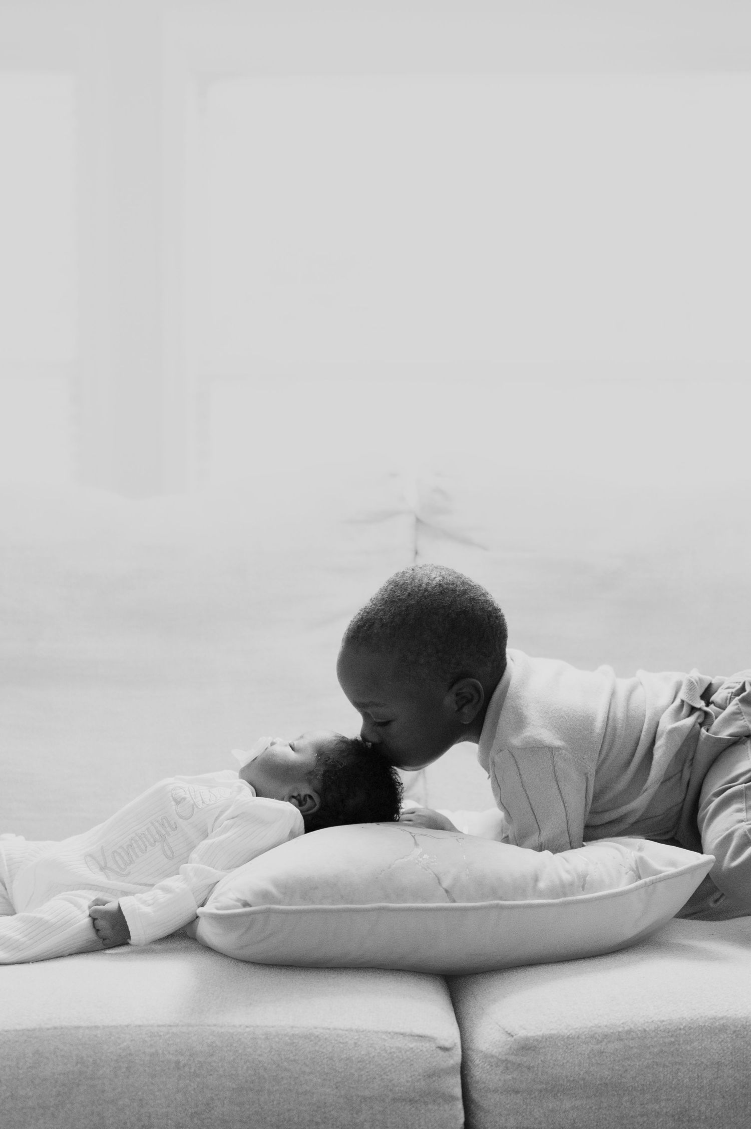 Child resting peacefully on white pillow in minimalist setting with soft lighting.