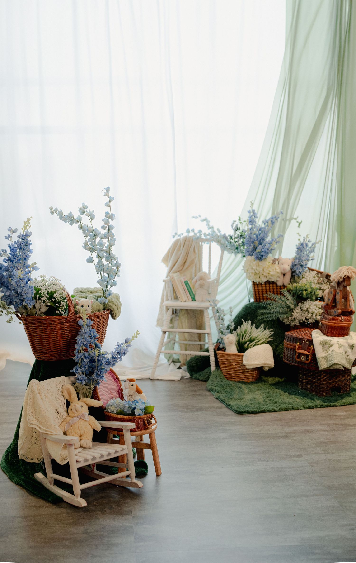 Vintage-style photo set with rocking chairs, blue flowers and soft green drapery against white backdrop.