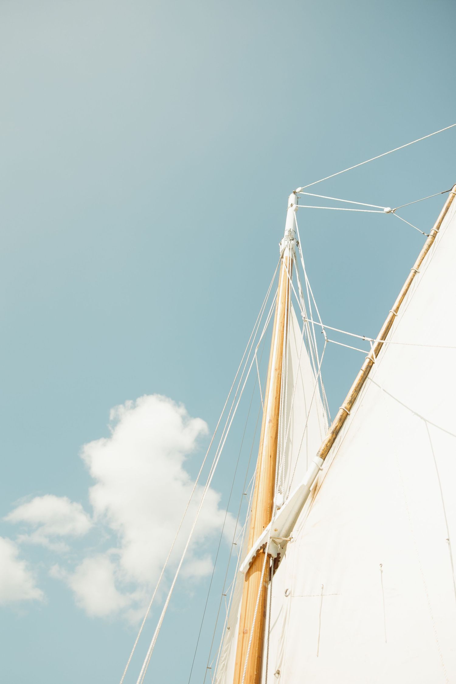 White sailboat masts against a bright blue sky with puffy clouds.