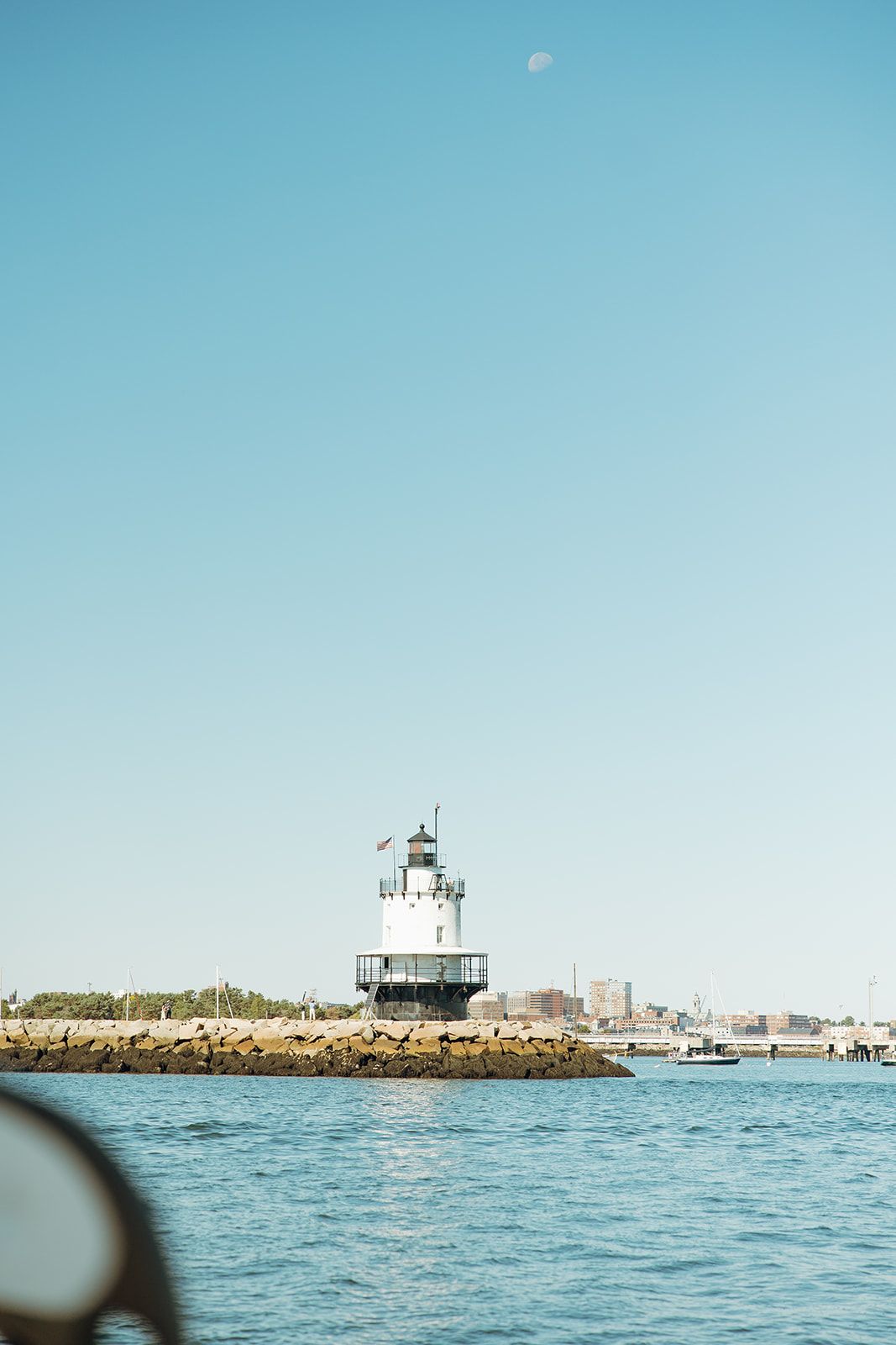 Lighthouse stands on rocky breakwater with calm blue waters and clear sky in nautical seascape.