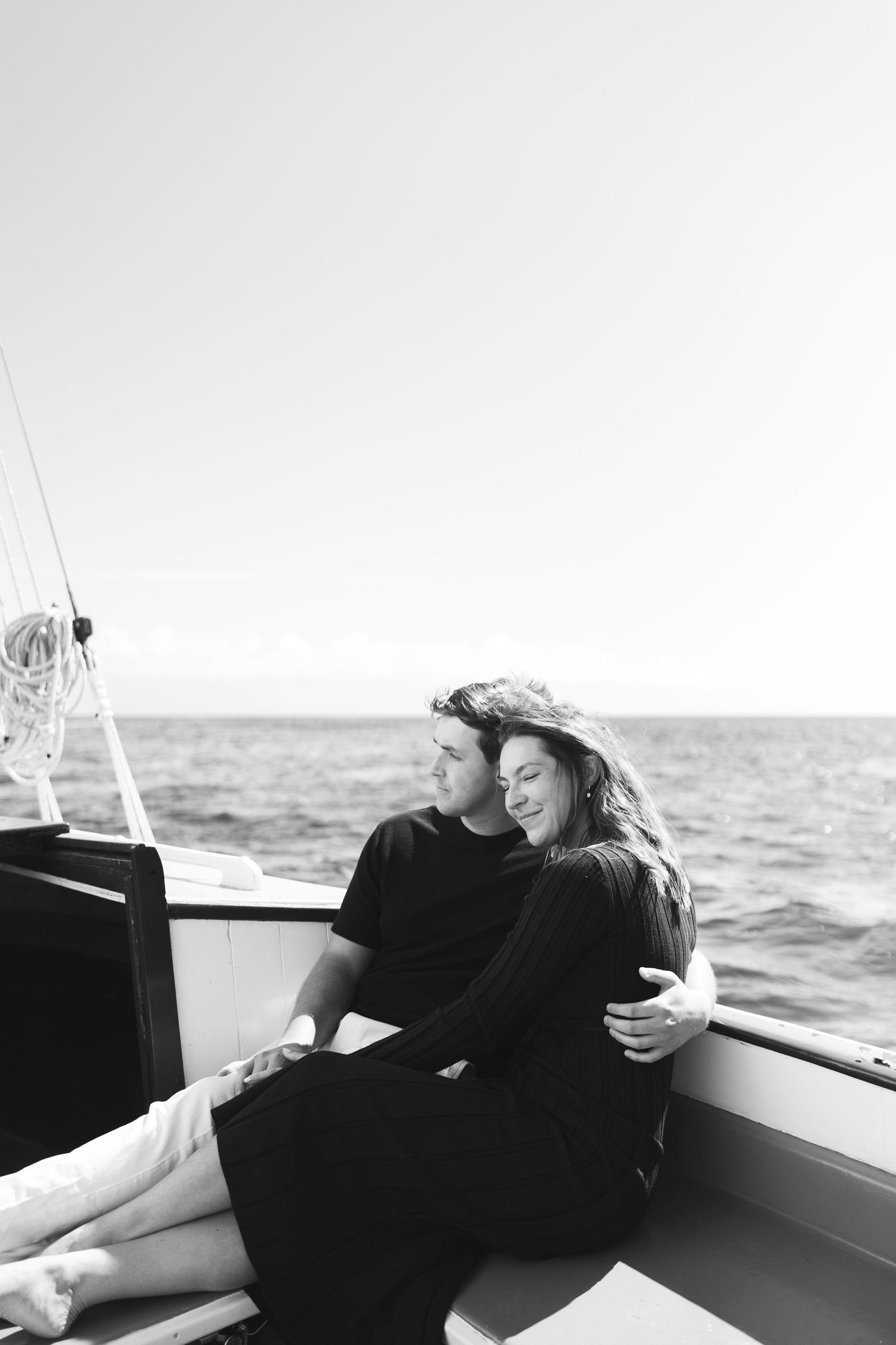 A person in black clothing relaxes on a boat deck while sailing on the ocean during a sunny day.