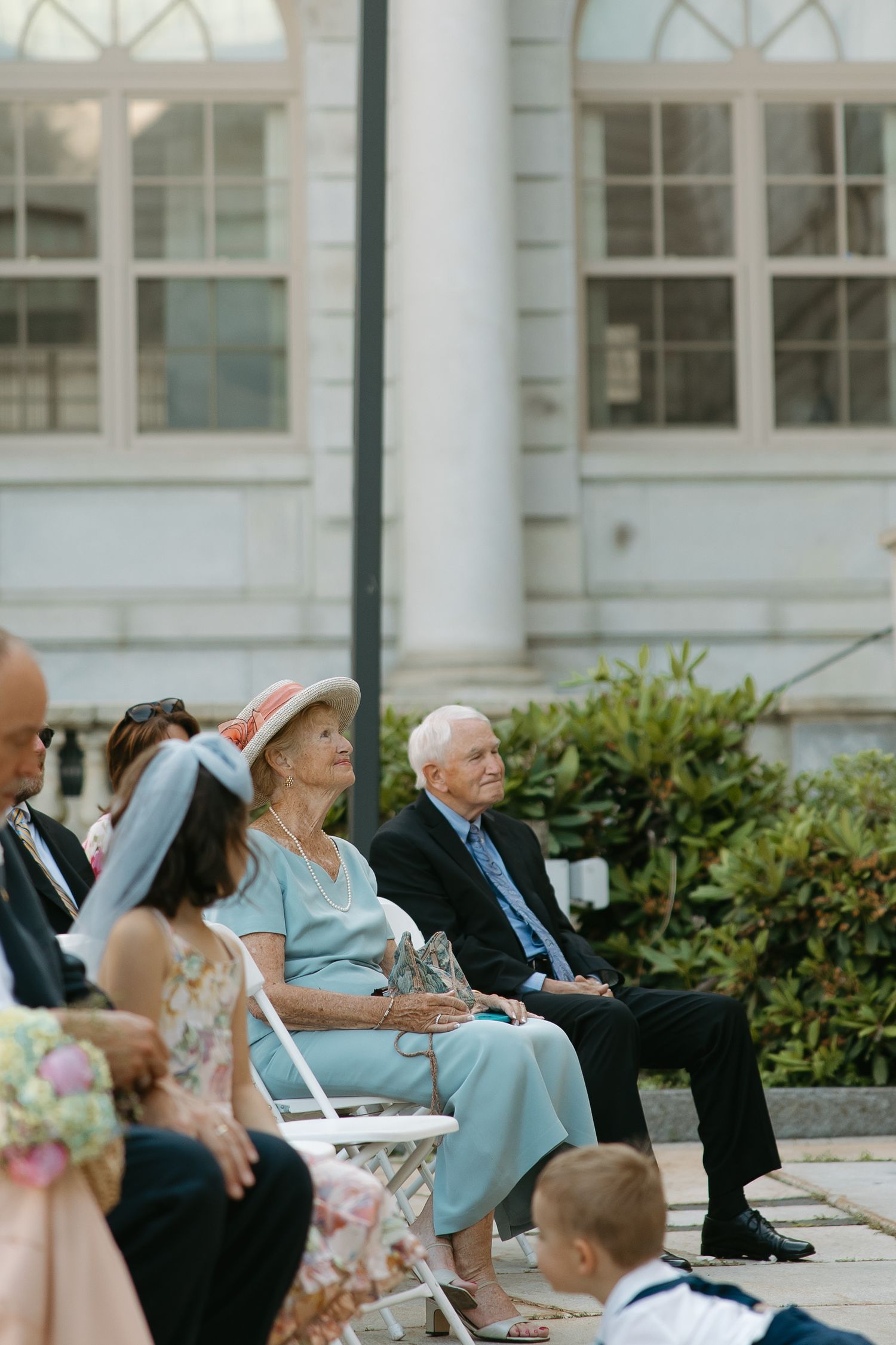 Wedding guests seated outdoors on white chairs during an elegant garden ceremony.