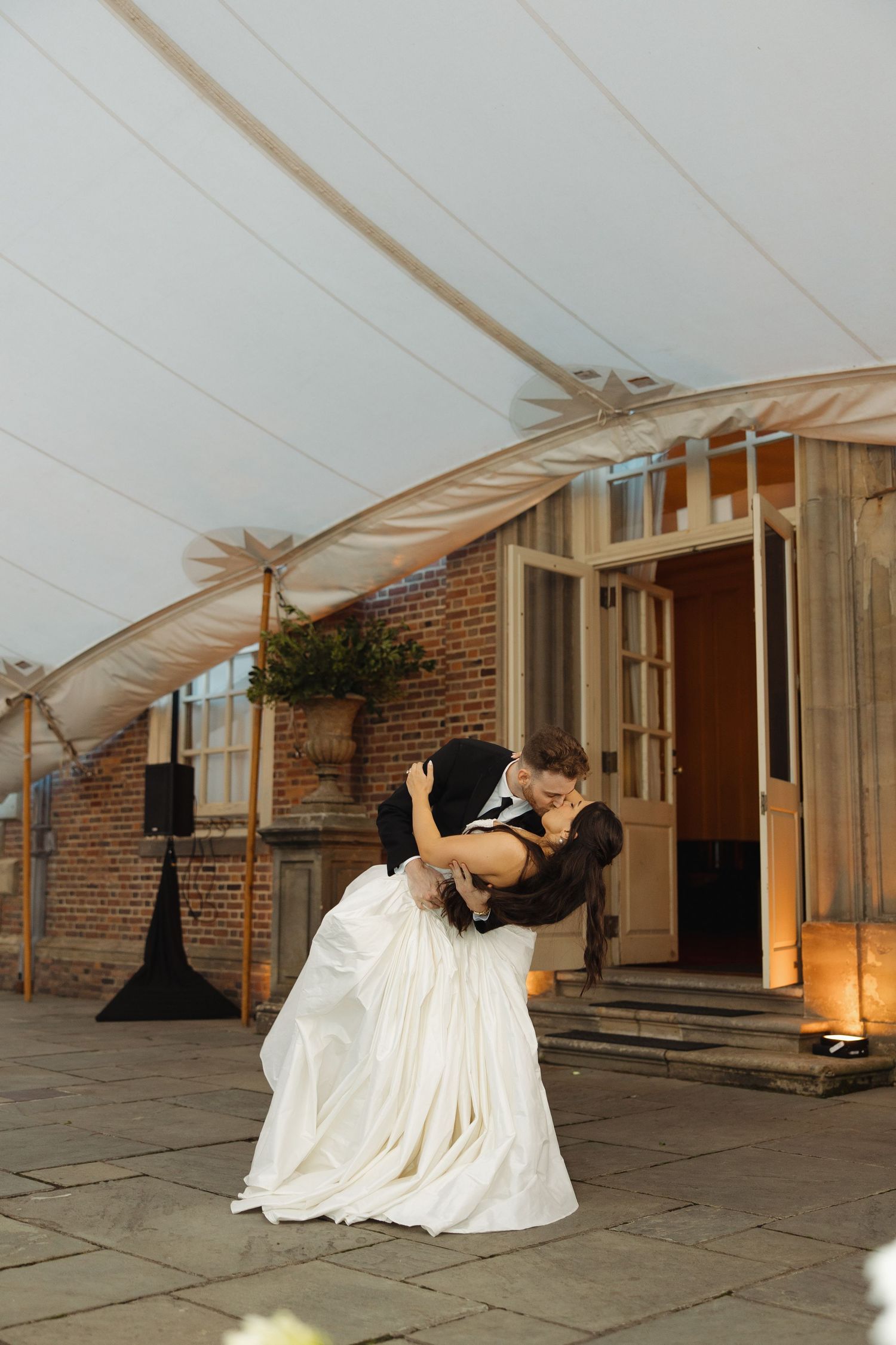 A figure in a flowing white dress performs an expressive dance movement sequence against a brick building exterior.