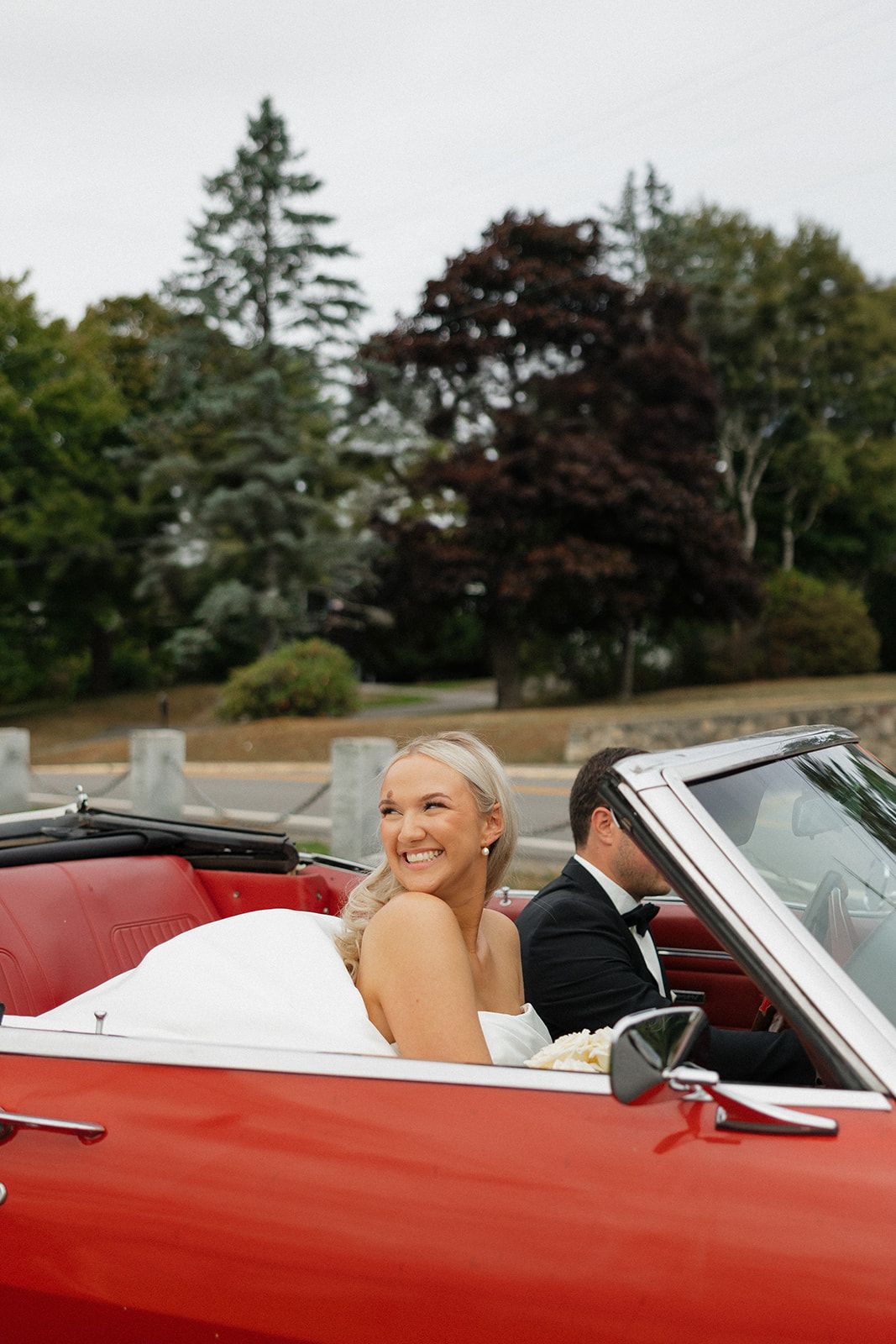 A red vintage convertible car parked outdoors with trees visible in the background.