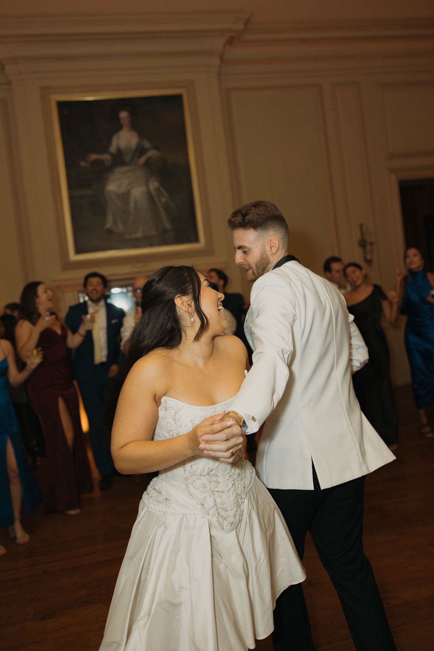 Couple shares their first dance at an elegant wedding reception with a vintage portrait hanging in the background.