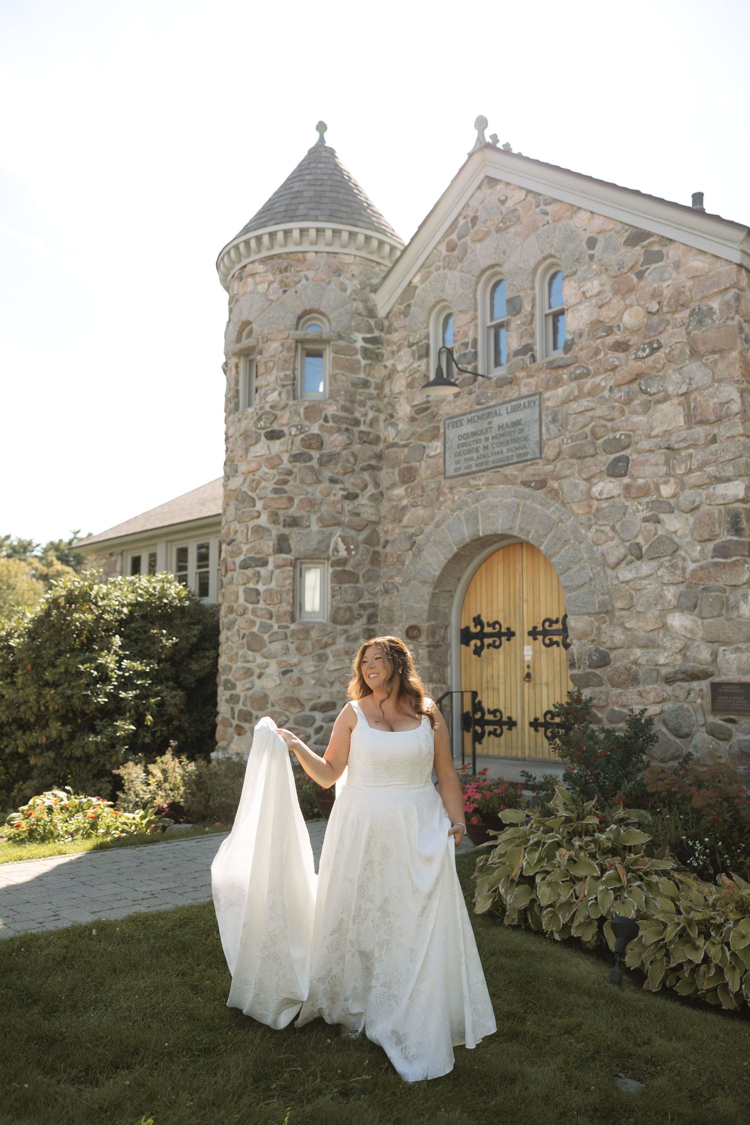 A flowing white wedding dress twirls against the backdrop of a stone castle-like building in natural sunlight.
