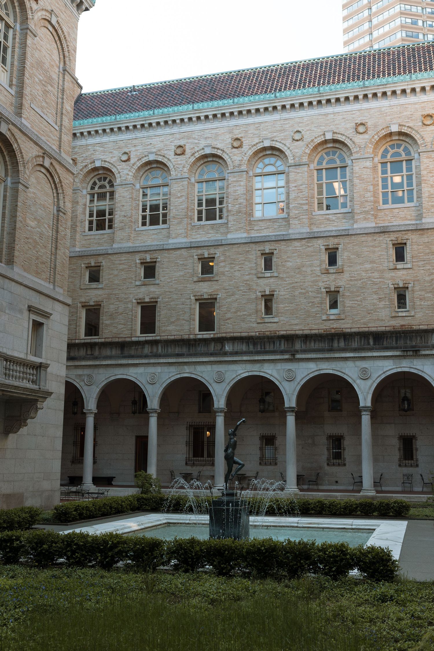 Historic stone building with arched colonnade and courtyard featuring a decorative fountain and manicured garden.