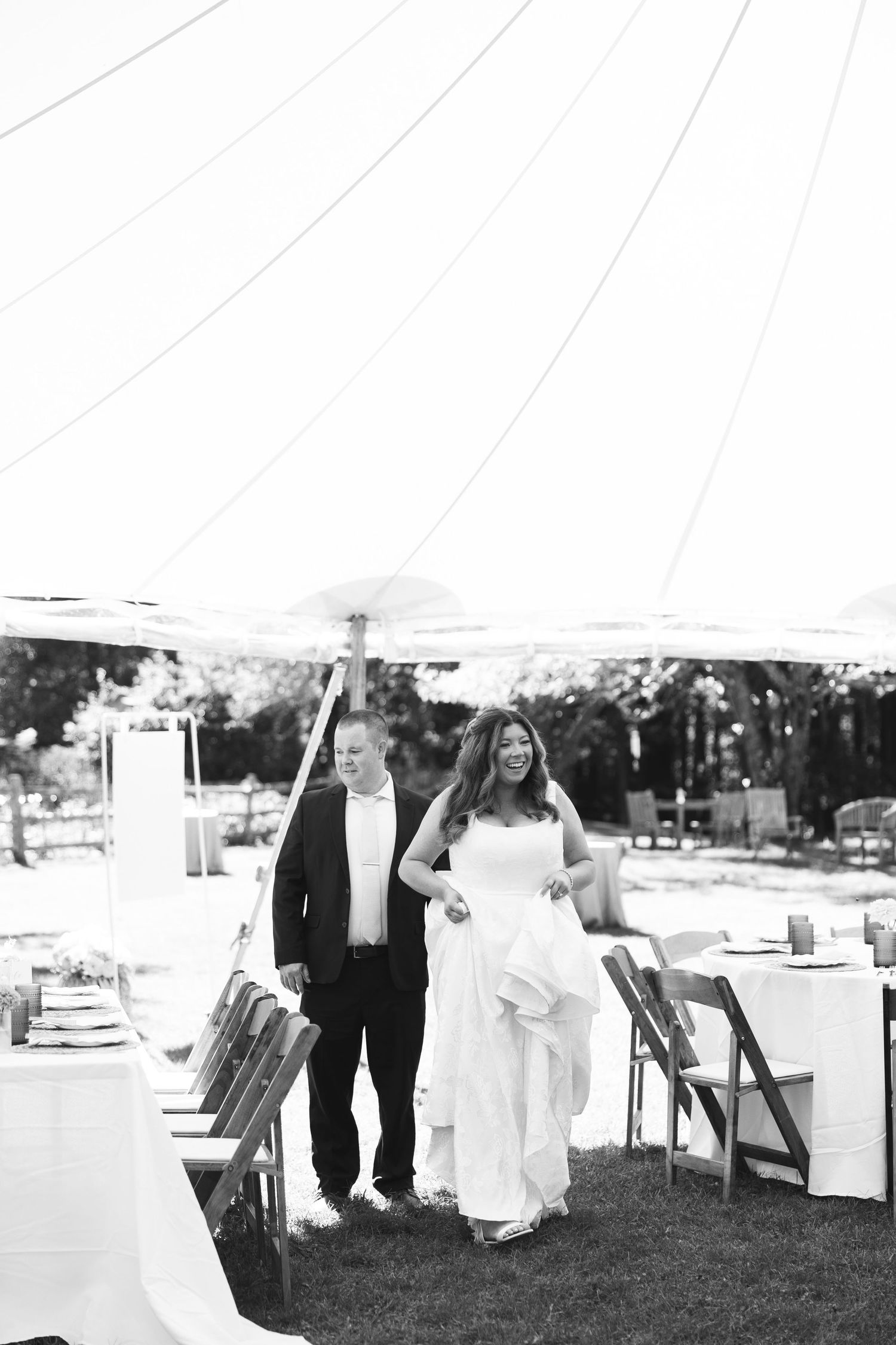 A black and white wedding reception scene outdoors with tables and chairs set up on grass.