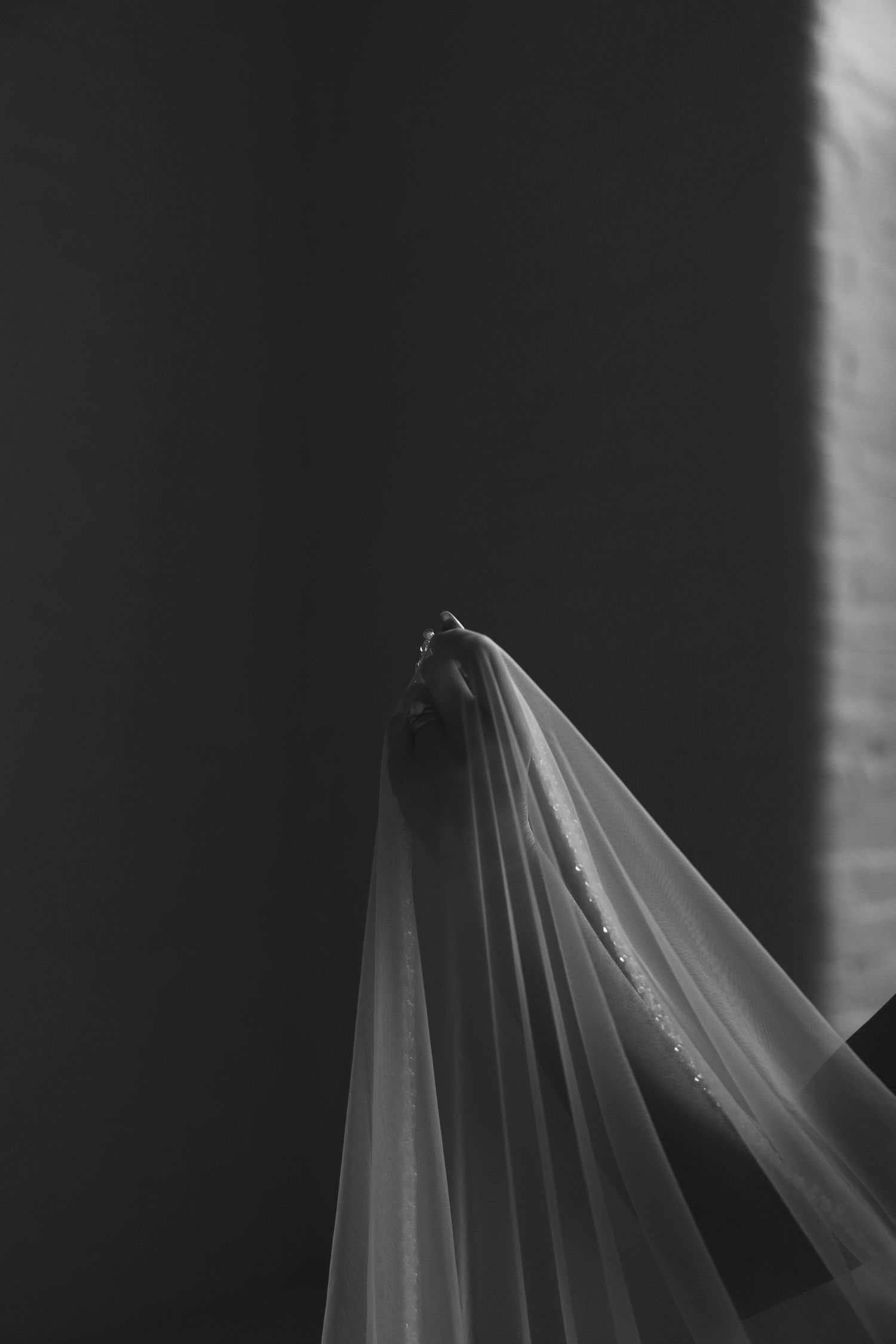 A close-up black and white photograph shows flowing white wedding veil fabric against a dark background.