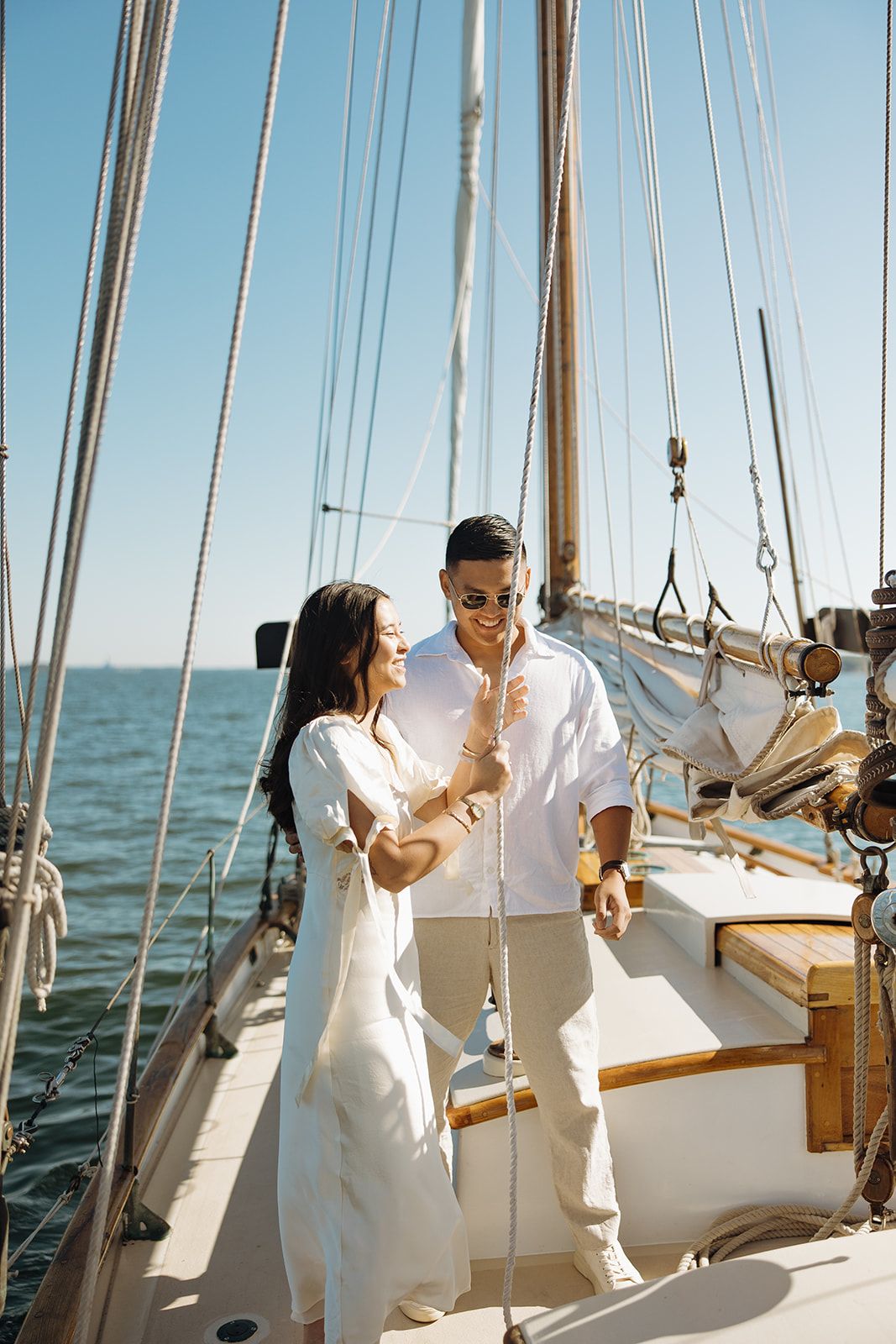 A couple in white outfits shares a romantic moment while sailing on a boat deck with ocean views in the background.