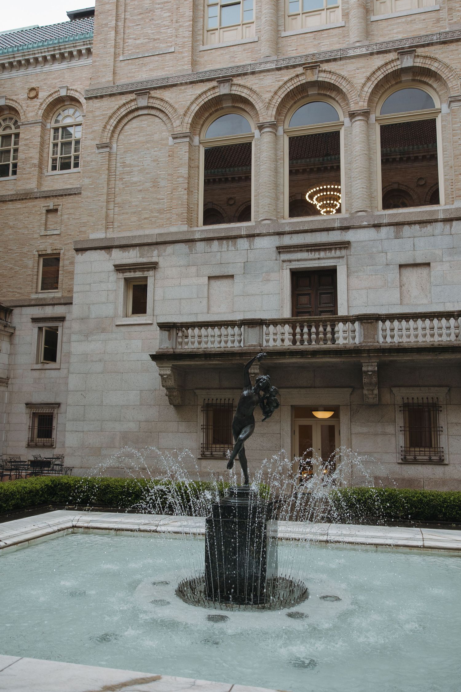 A series of fountains with water features in front of a classical stone building with arched windows and columns.