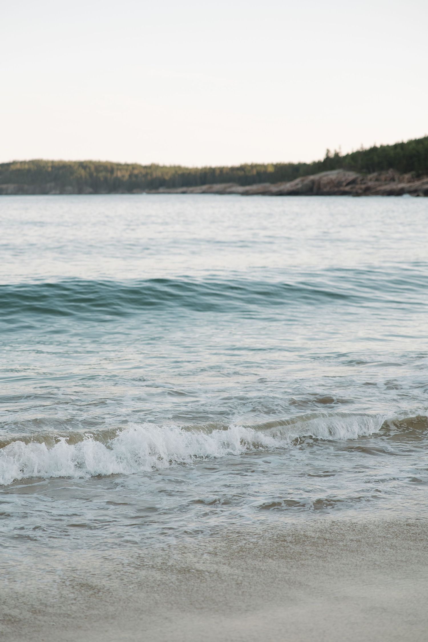 Serene coastal landscape with gentle waves rolling onto a sandy beach at sunset.