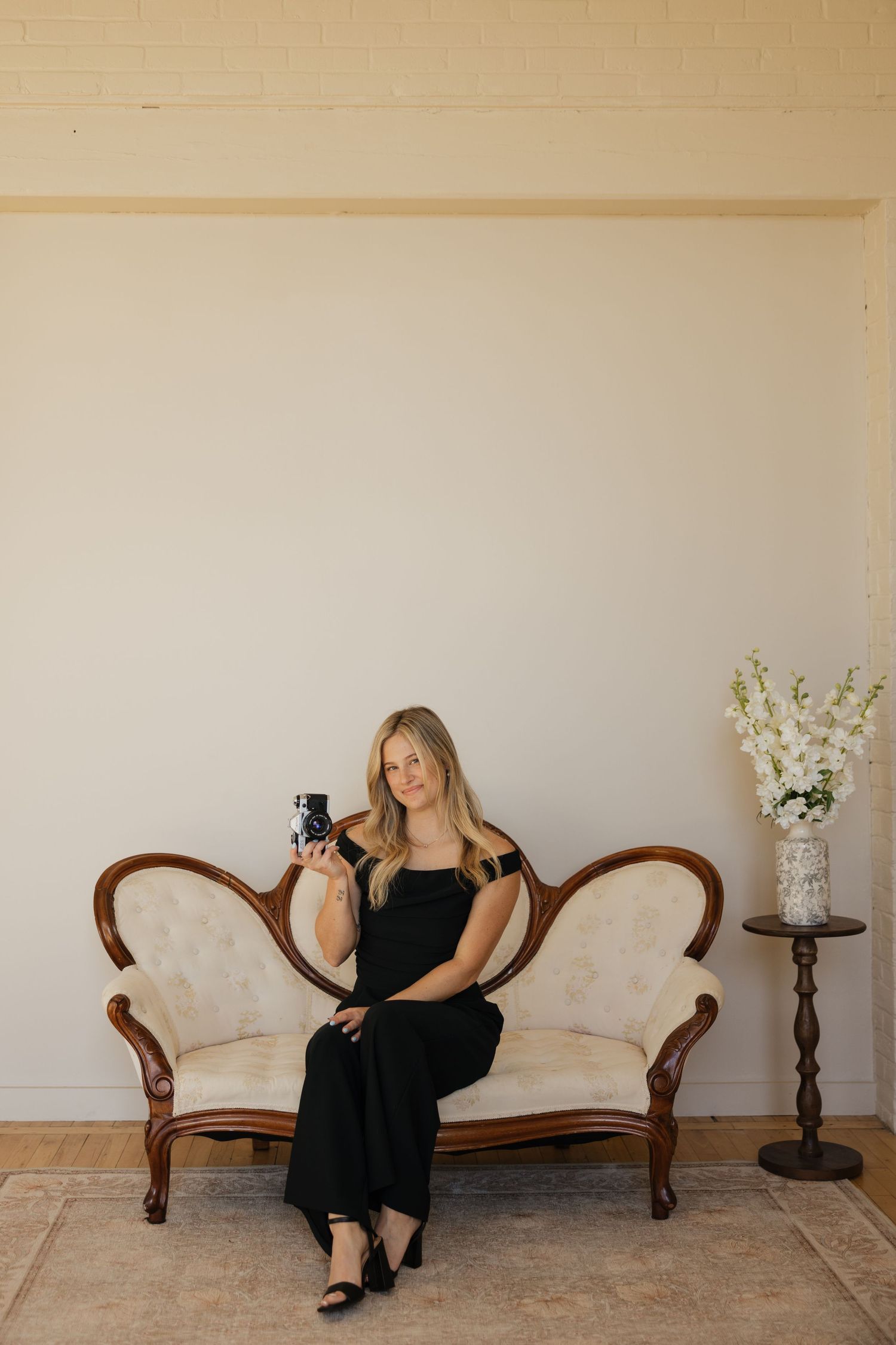 Photography session setup with antique furniture and floral decor against neutral wall.