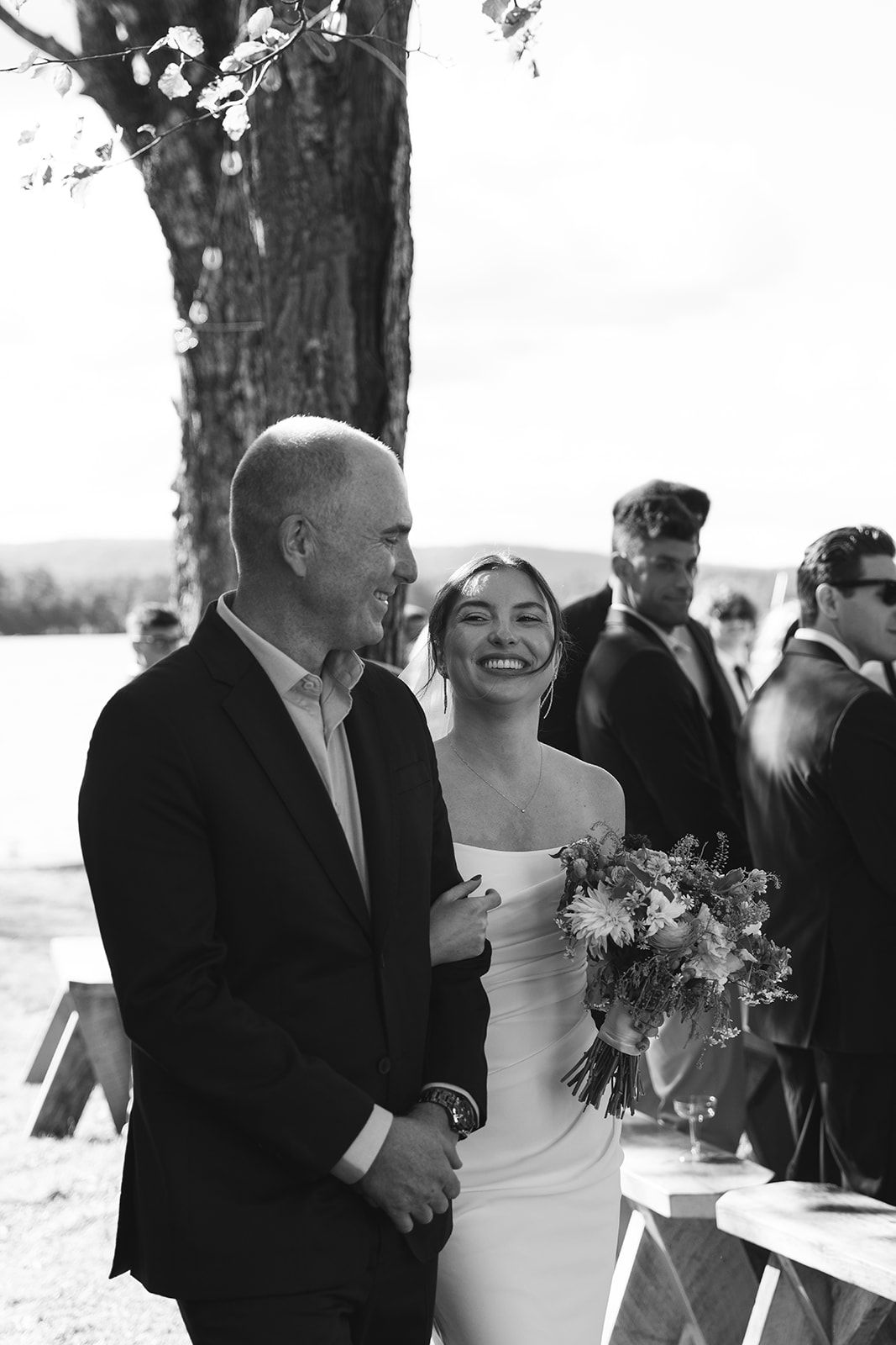 A black and white outdoor wedding photo showing a couple sharing a joyful moment under a tree.