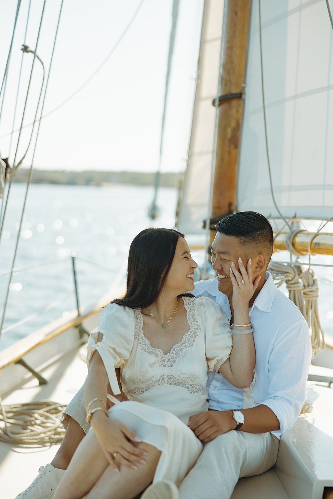 A couple in white outfits shares tender moments on a bright sunlit porch with wooden beams.