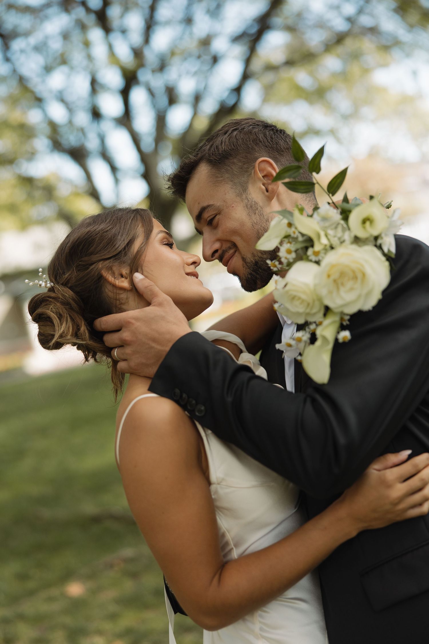 A romantic outdoor wedding moment captured on a grassy hillside with white roses in the bouquet.