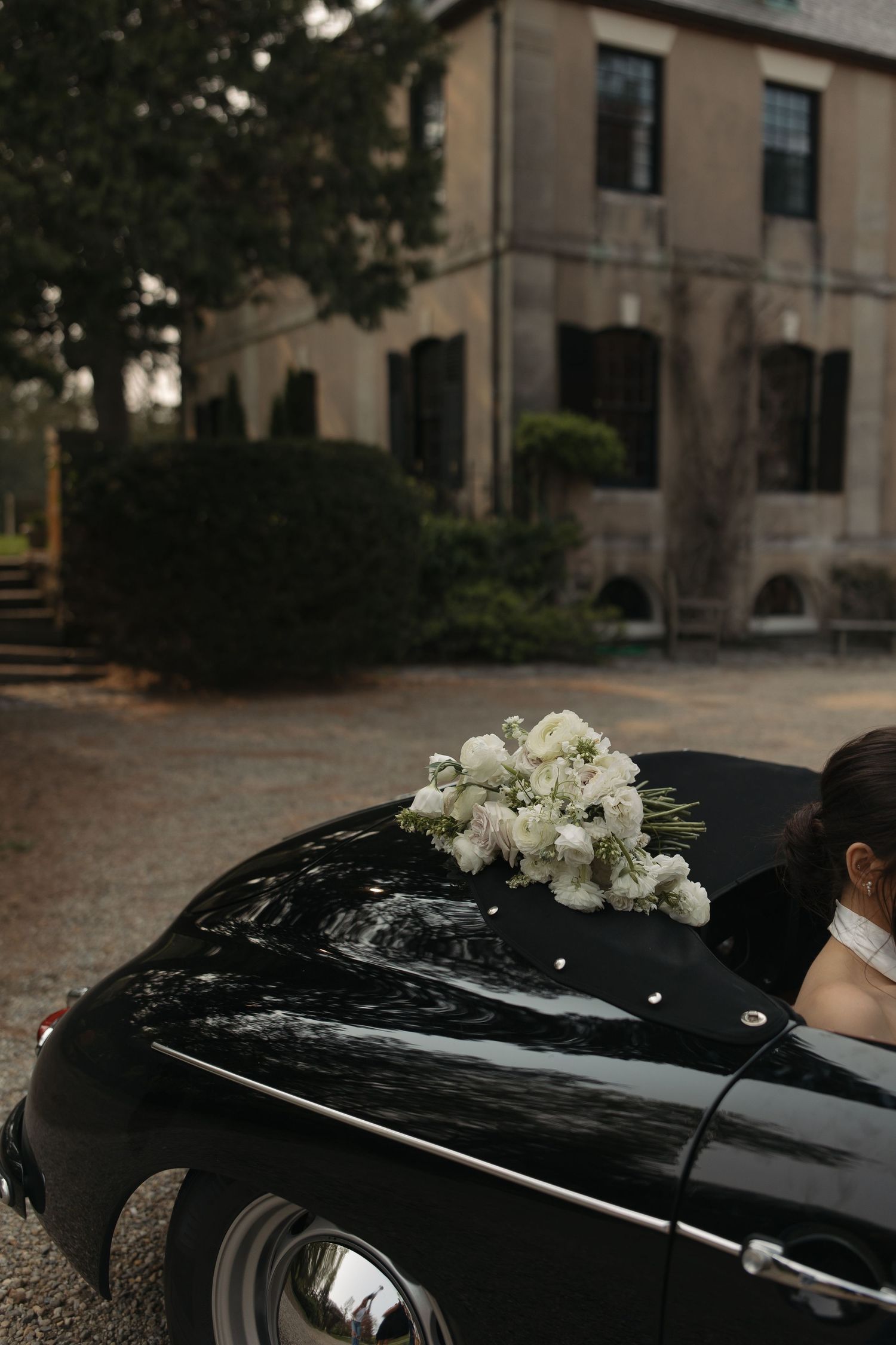 White roses decorate the roof of a black luxury car parked outside a building.