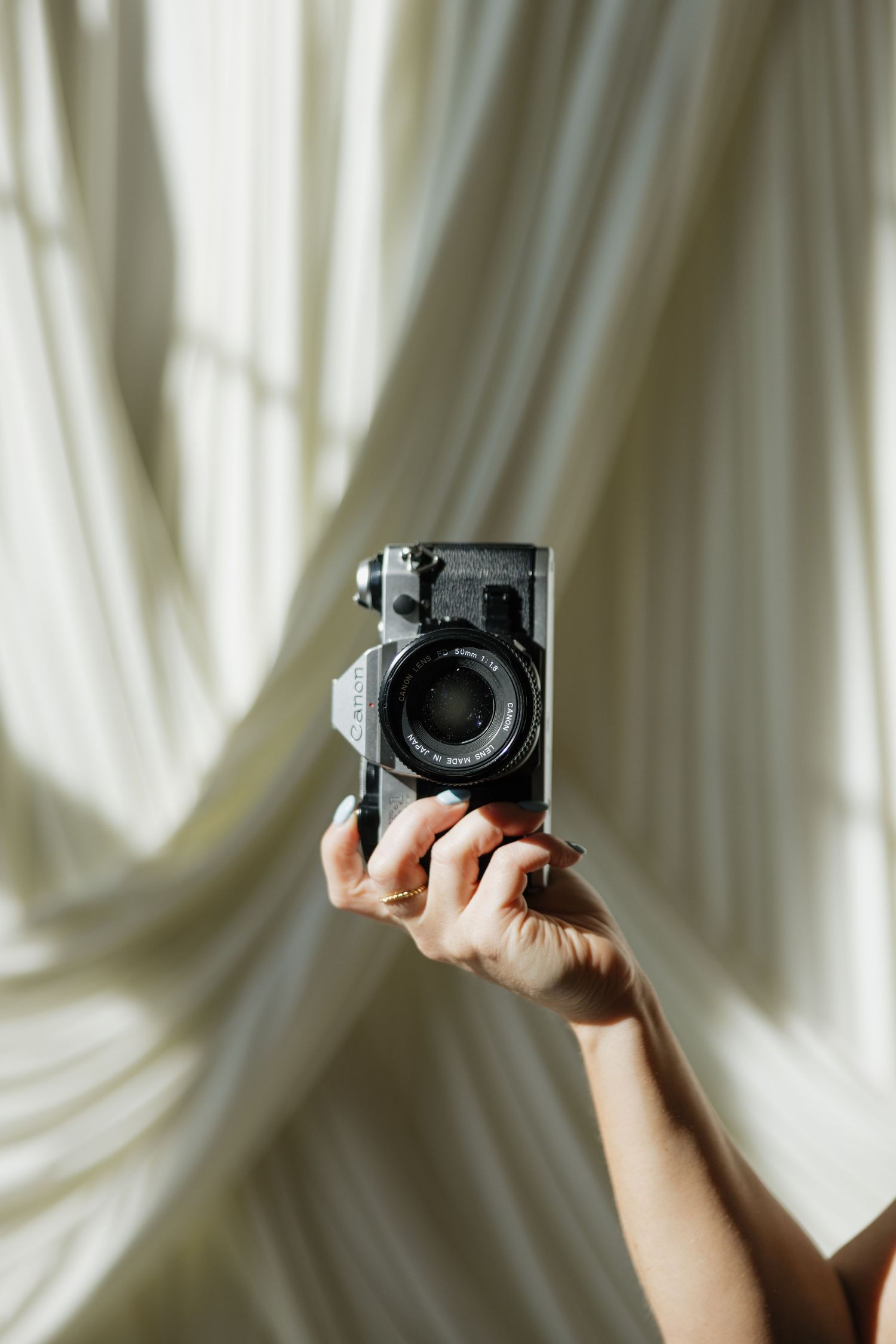 Hands holding up a vintage camera against flowing white fabric backdrop.
