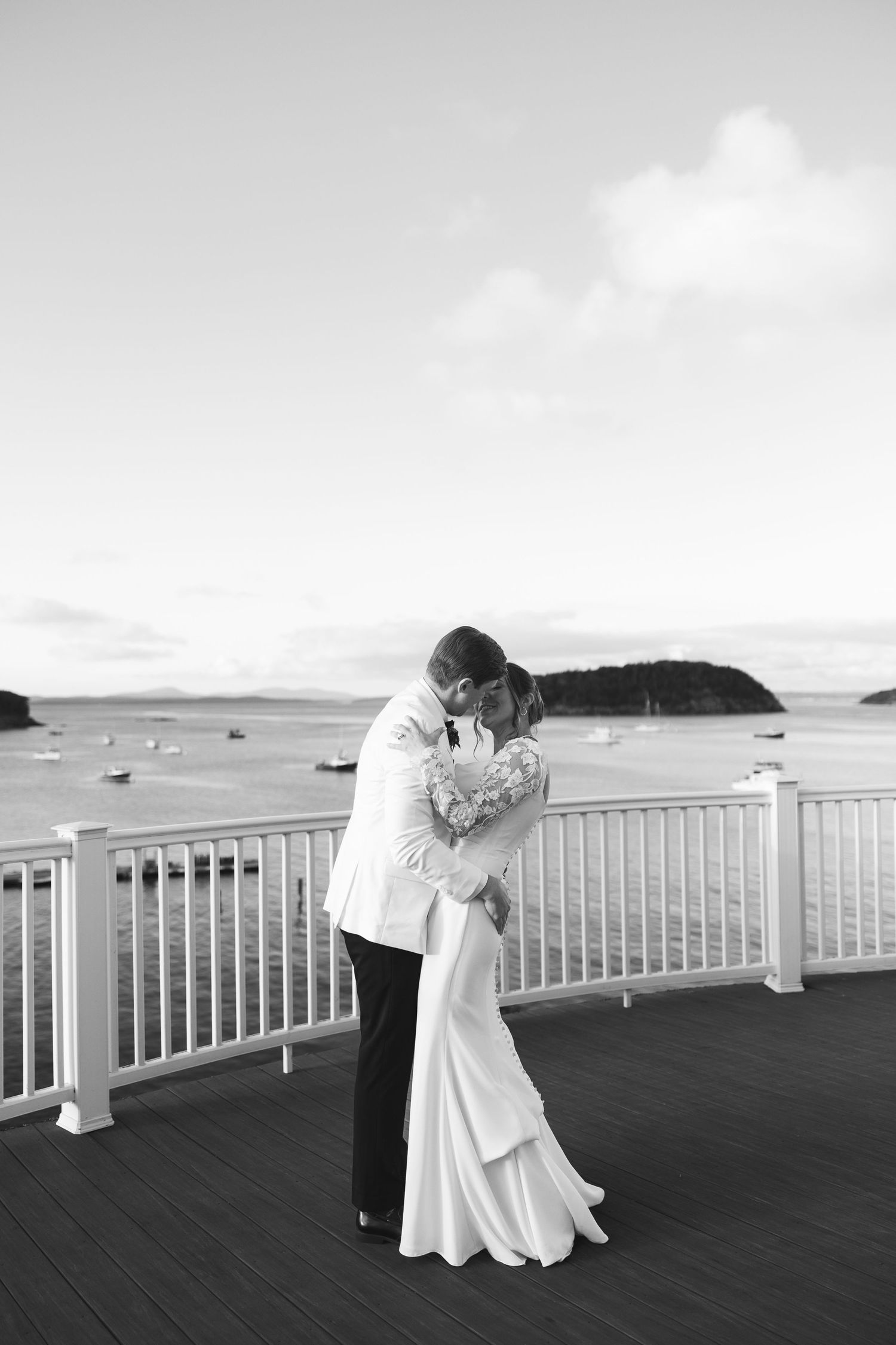 A romantic couple shares an intimate moment on a seaside deck with ocean and island views in the background.