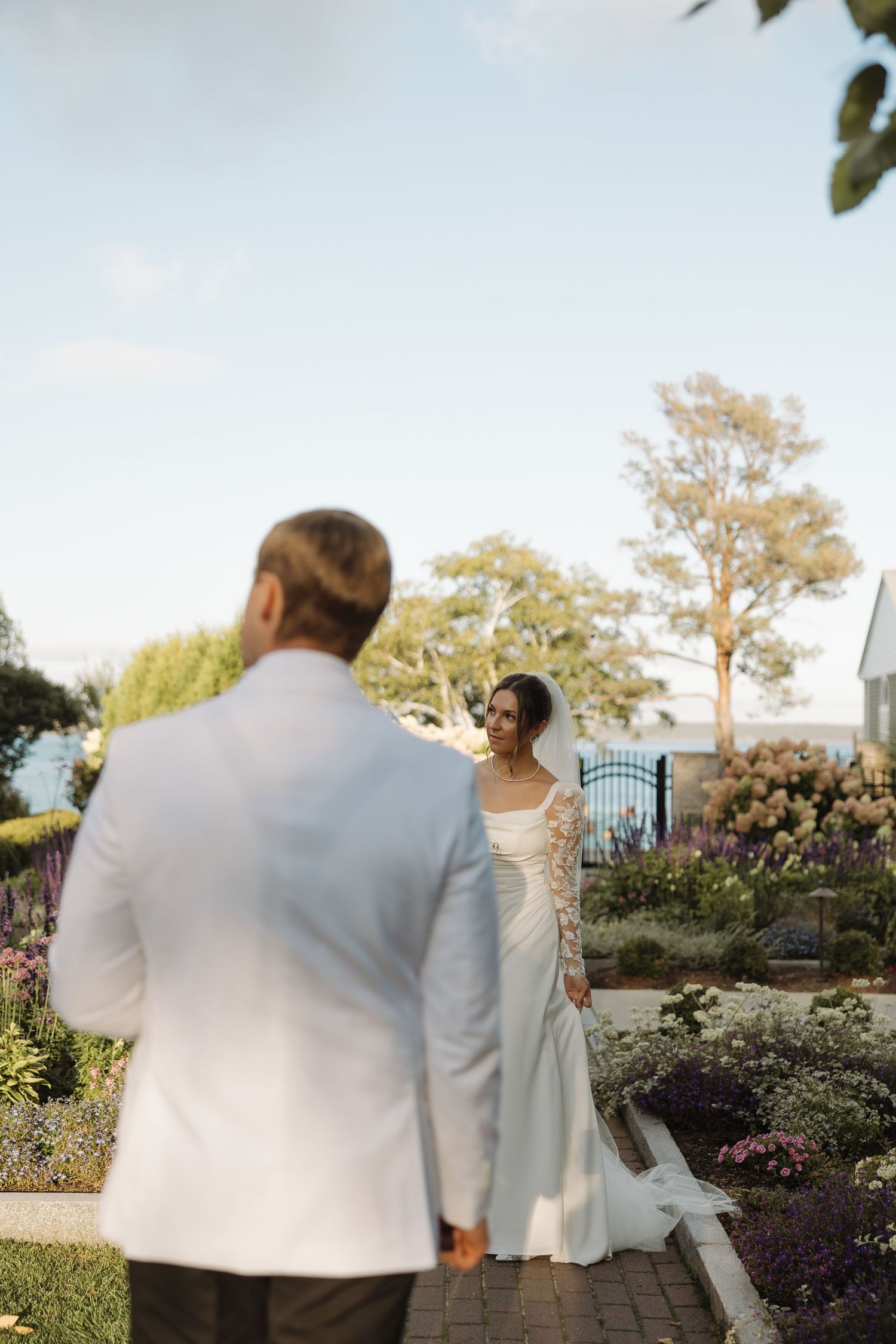 A couple in wedding attire walks together through a beautiful garden path during golden hour.