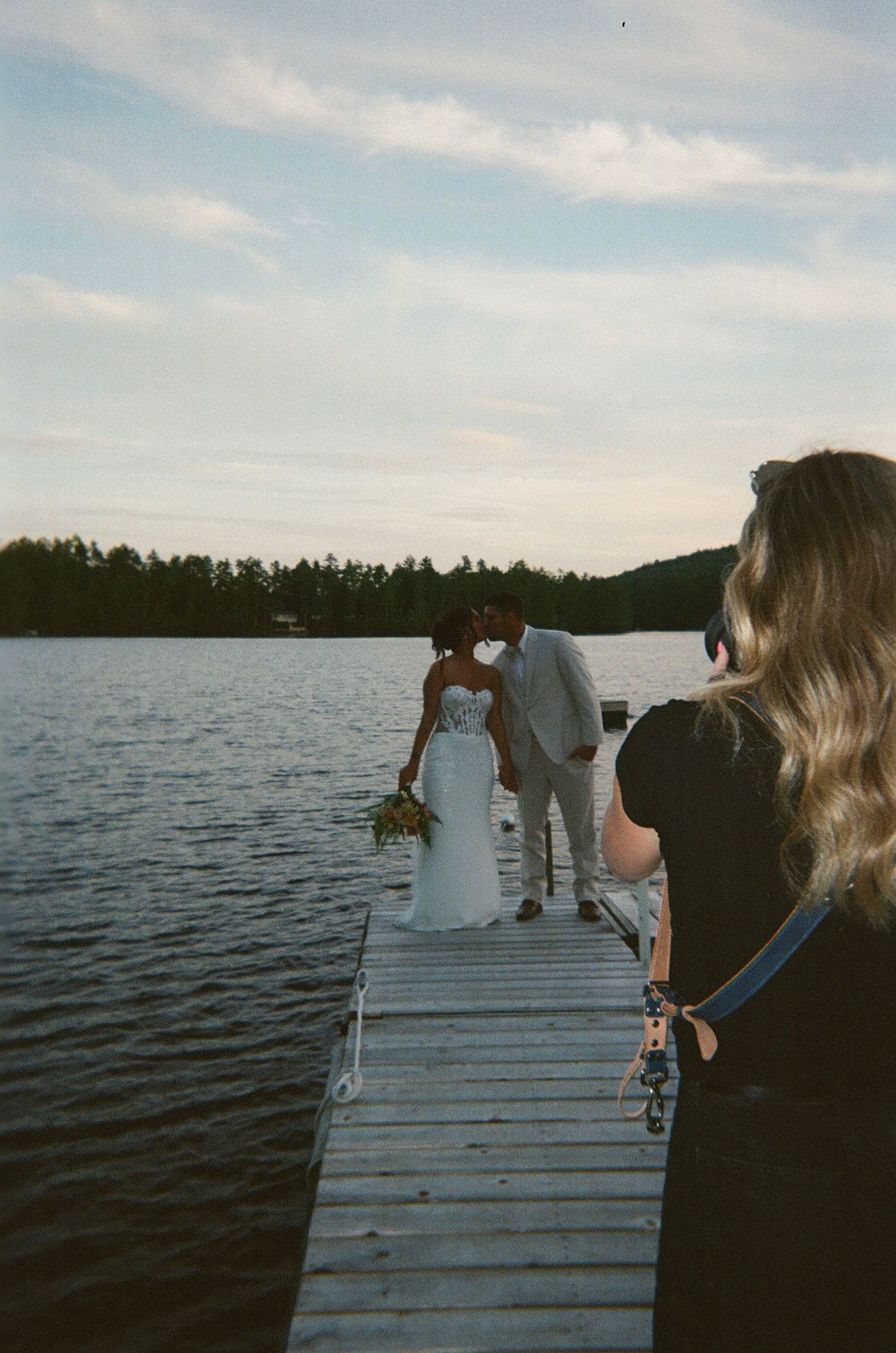 Wedding photography being captured on a wooden dock overlooking a peaceful lake.