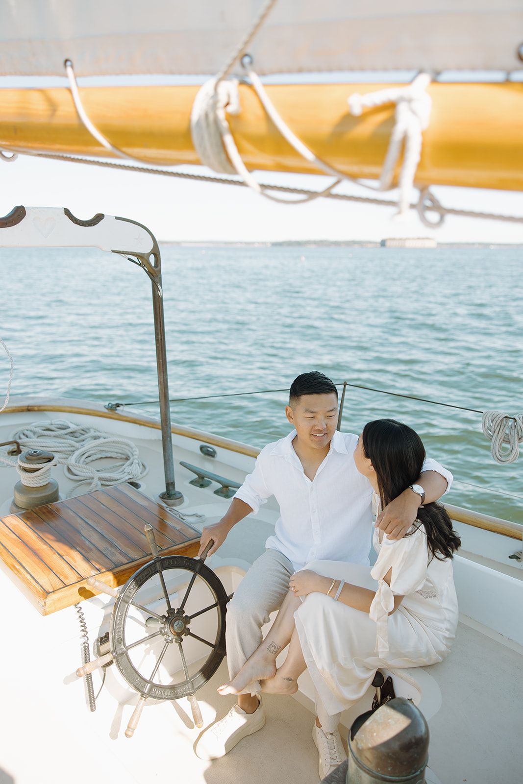 A romantic couple in white outfits shares intimate moments on a boat deck with a ship's wheel visible.