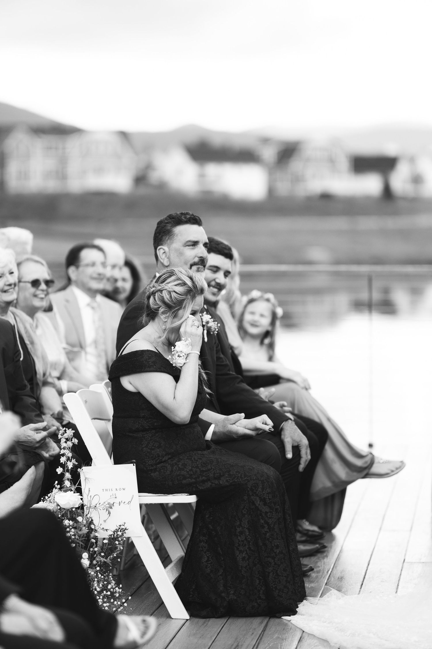 Wedding guests share joyful laughter while sitting together outdoors in black and white photography.