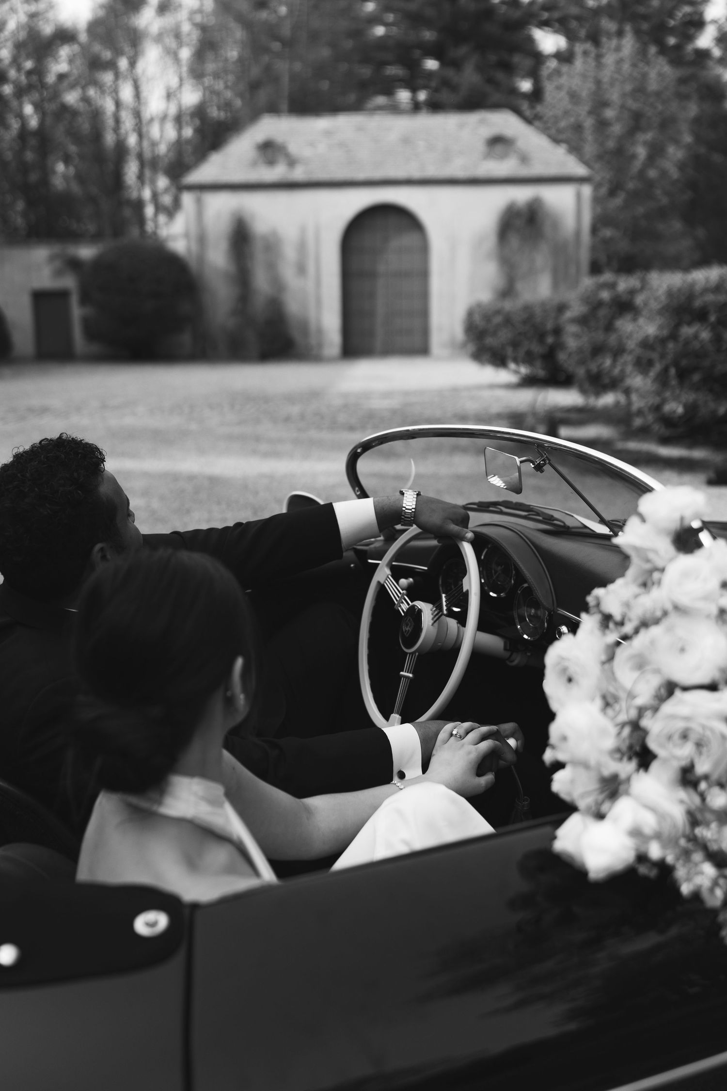A vintage black and white photo series showing someone driving a classic convertible car with flowers in the back seat.
