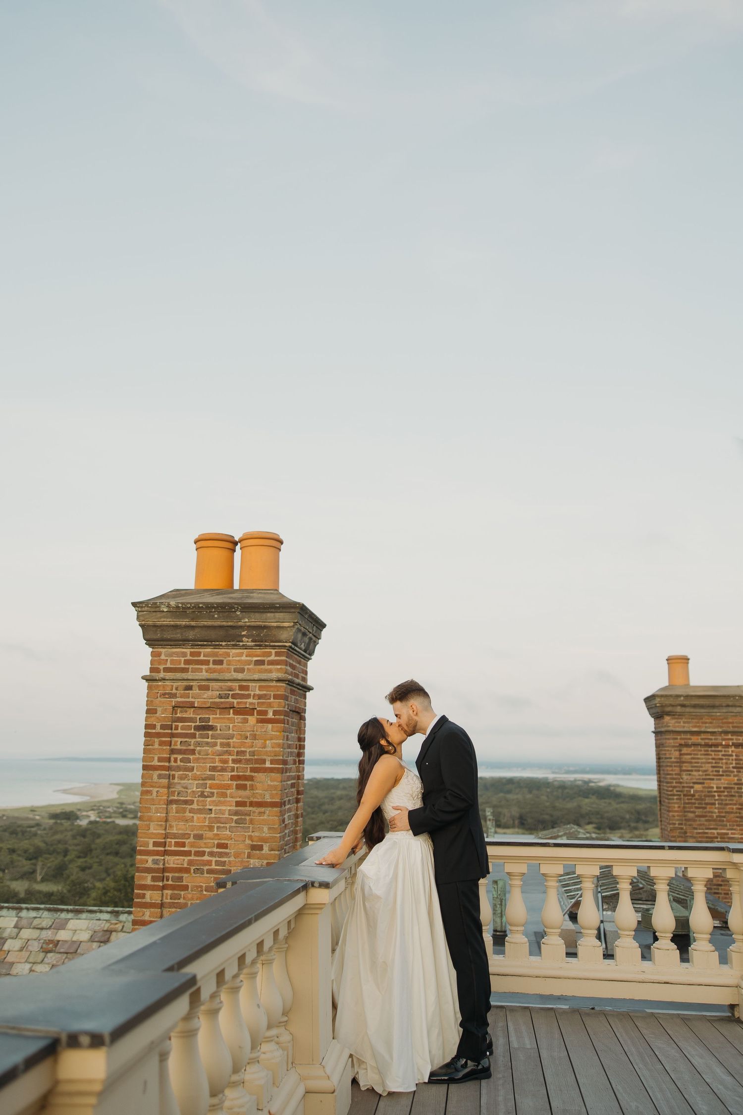 A romantic couple shares an intimate moment on a rooftop terrace overlooking a scenic landscape at sunset.