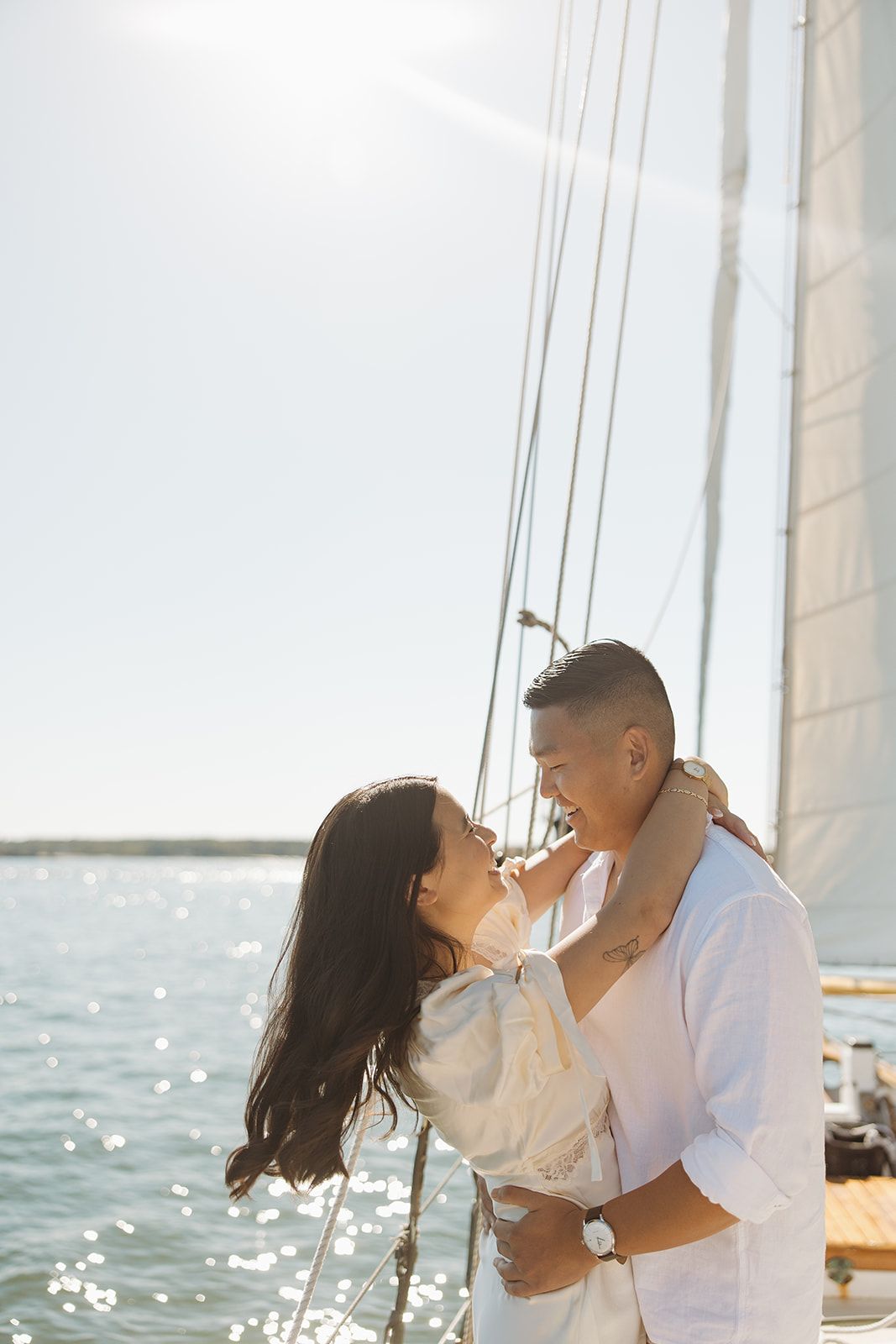 Romantic couple embraces on a sunny boat deck with sparkling ocean waters in the background.