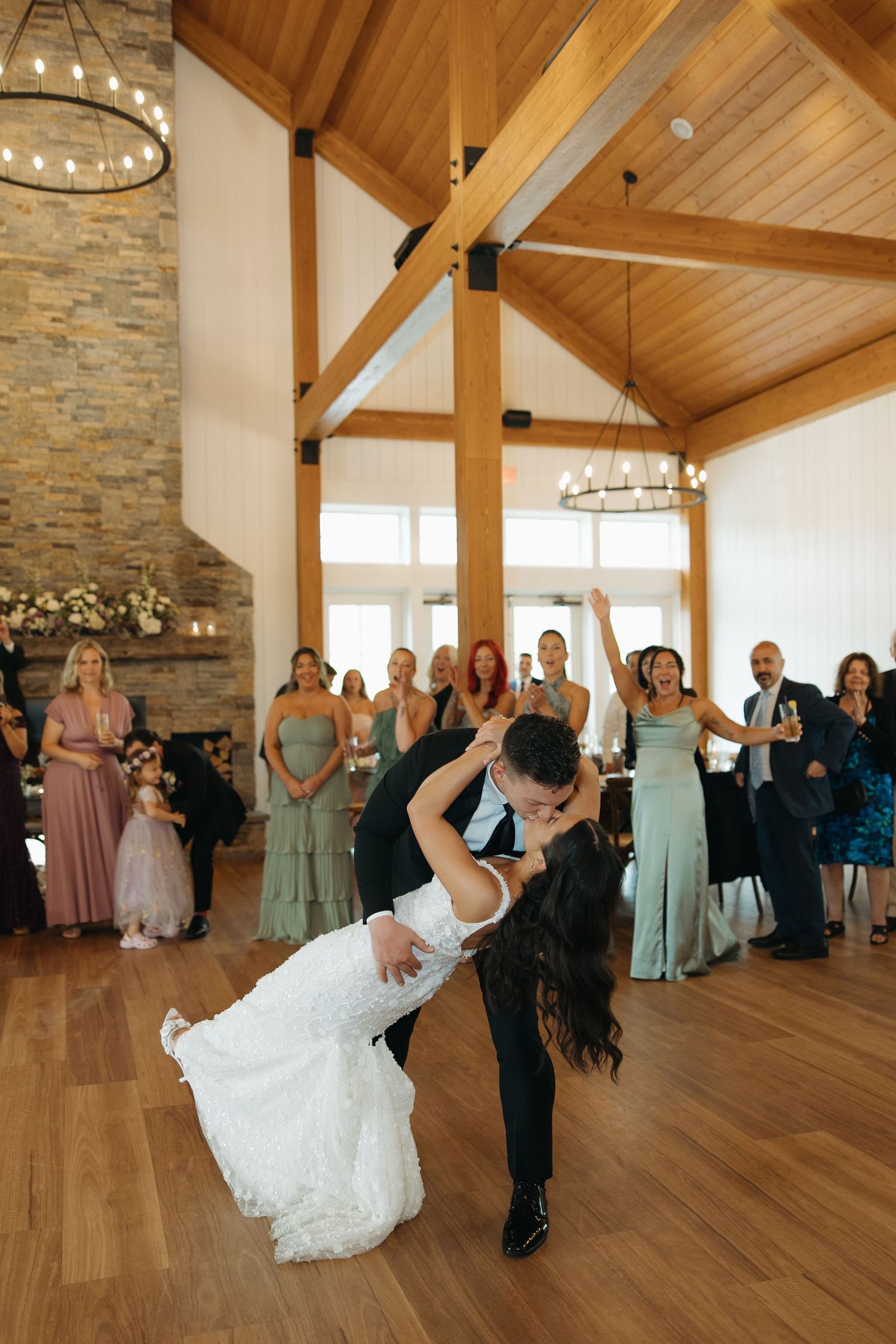 A couple performs a dramatic dip dance move on a wooden floor in an elegant venue with exposed beams and stone walls.