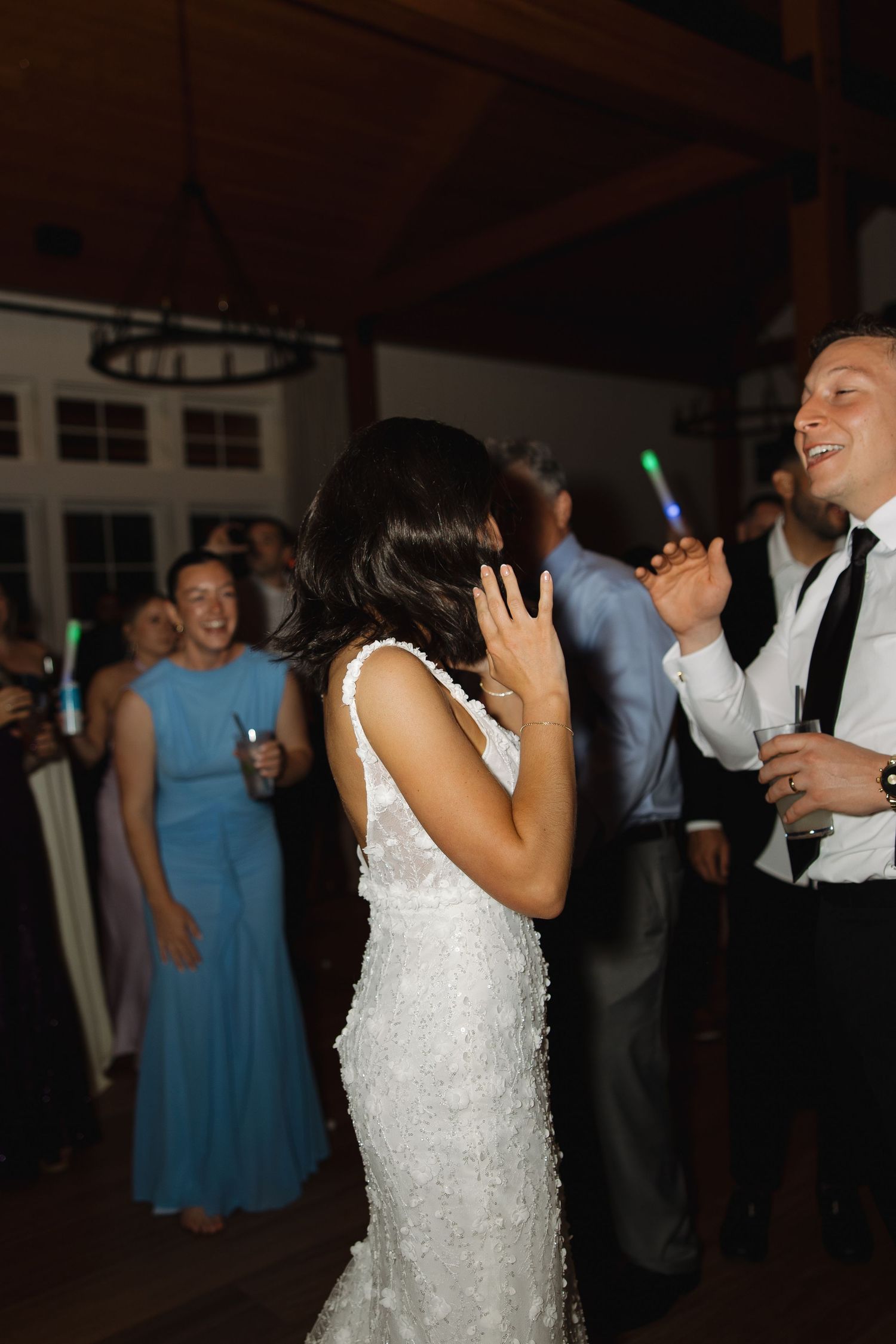Wedding guests dance and celebrate on a dimly lit dance floor with bridesmaids in blue dresses visible in the background.