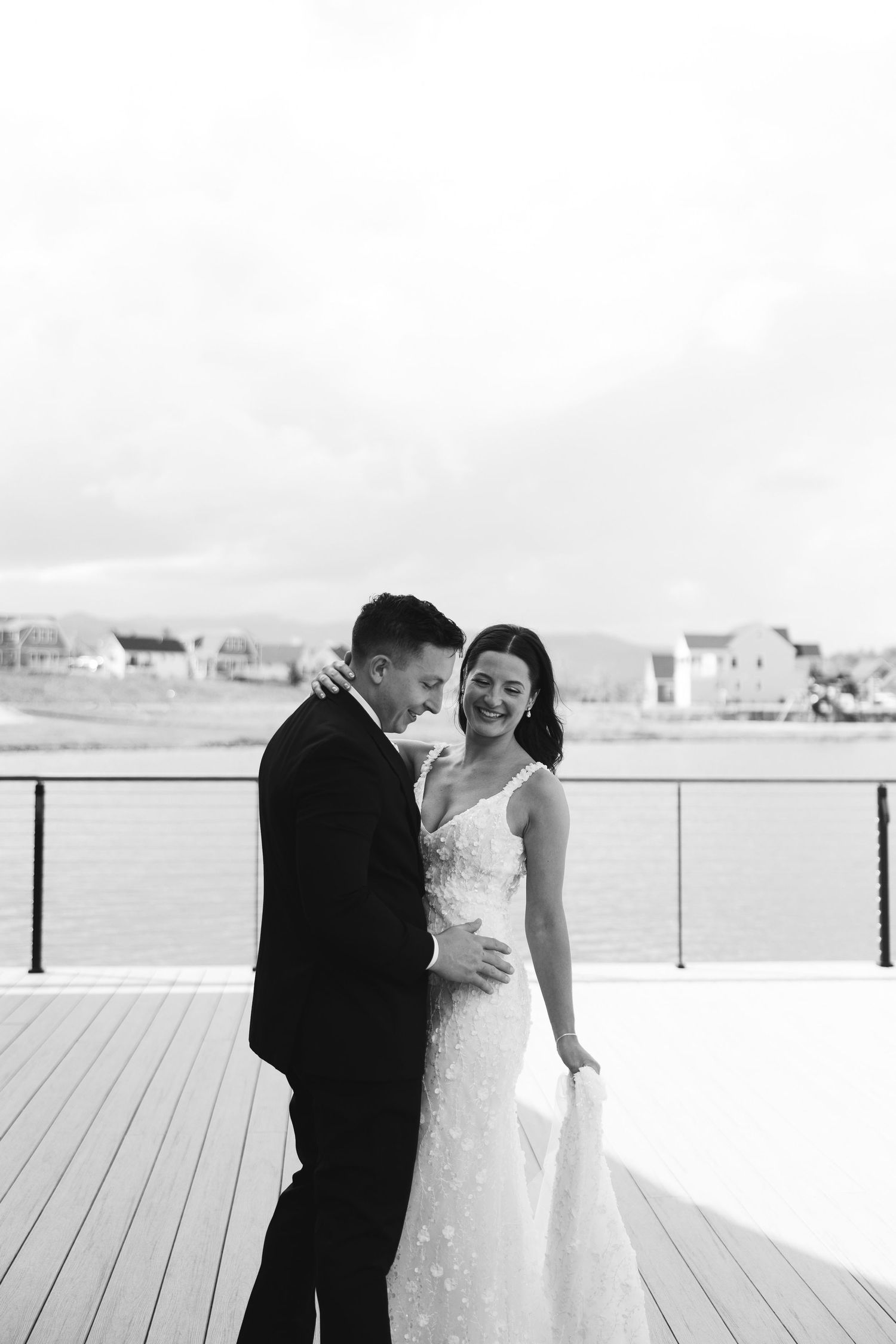 A romantic black and white wedding photo of a couple sharing an intimate moment on a deck overlooking houses.