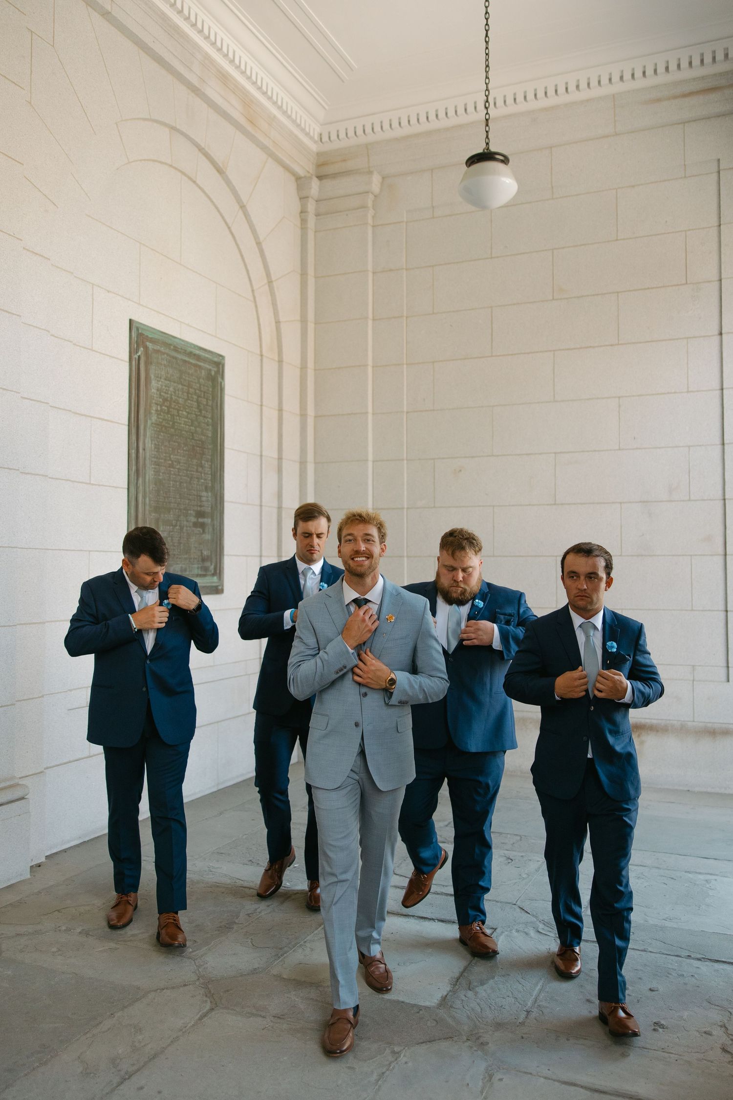 Groomsmen in blue suits perform synchronized dance moves in a sequence of photos inside a white room.