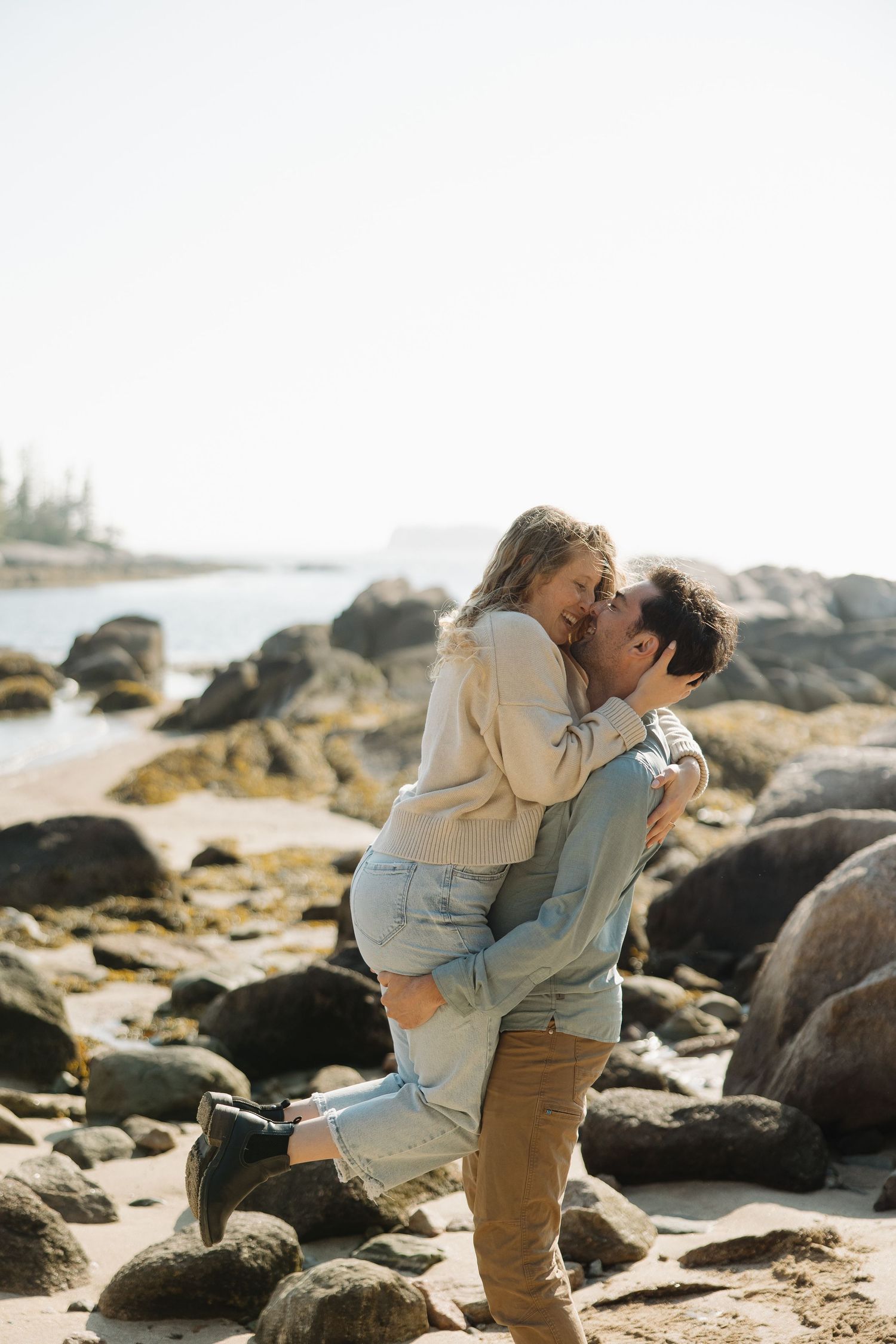 A romantic couple embraces on a rocky beach during a sunset photoshoot.