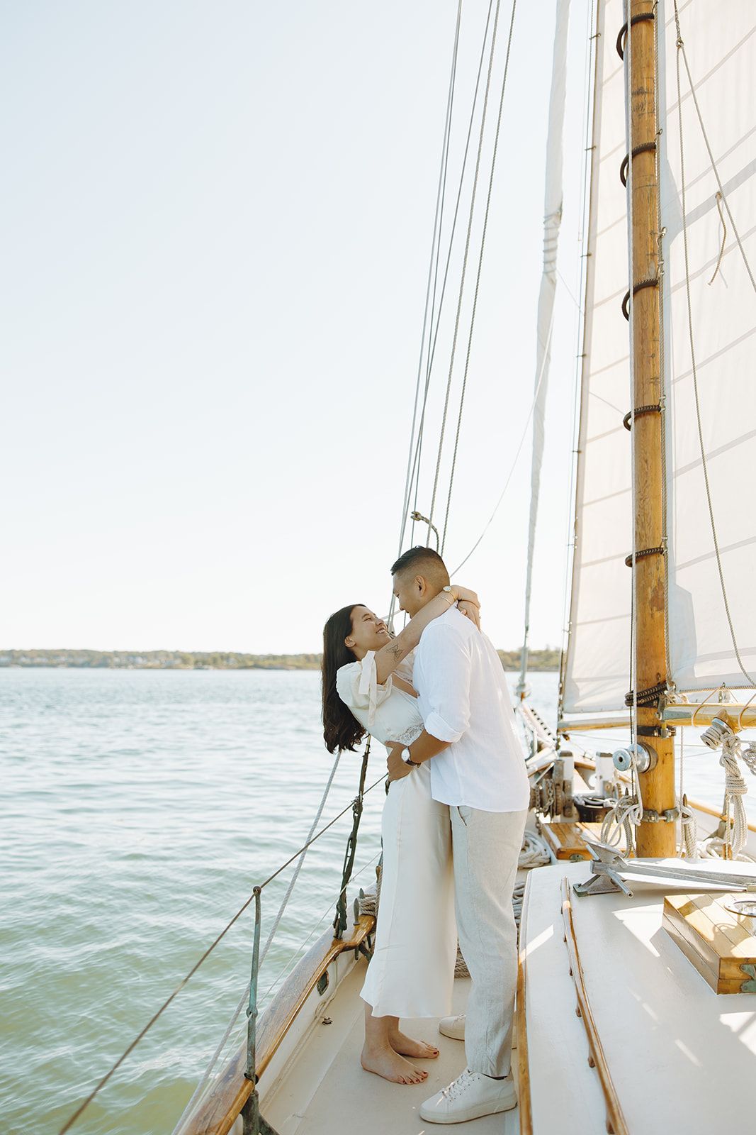 A couple shares romantic moments on a sailboat deck against a scenic waterfront backdrop.