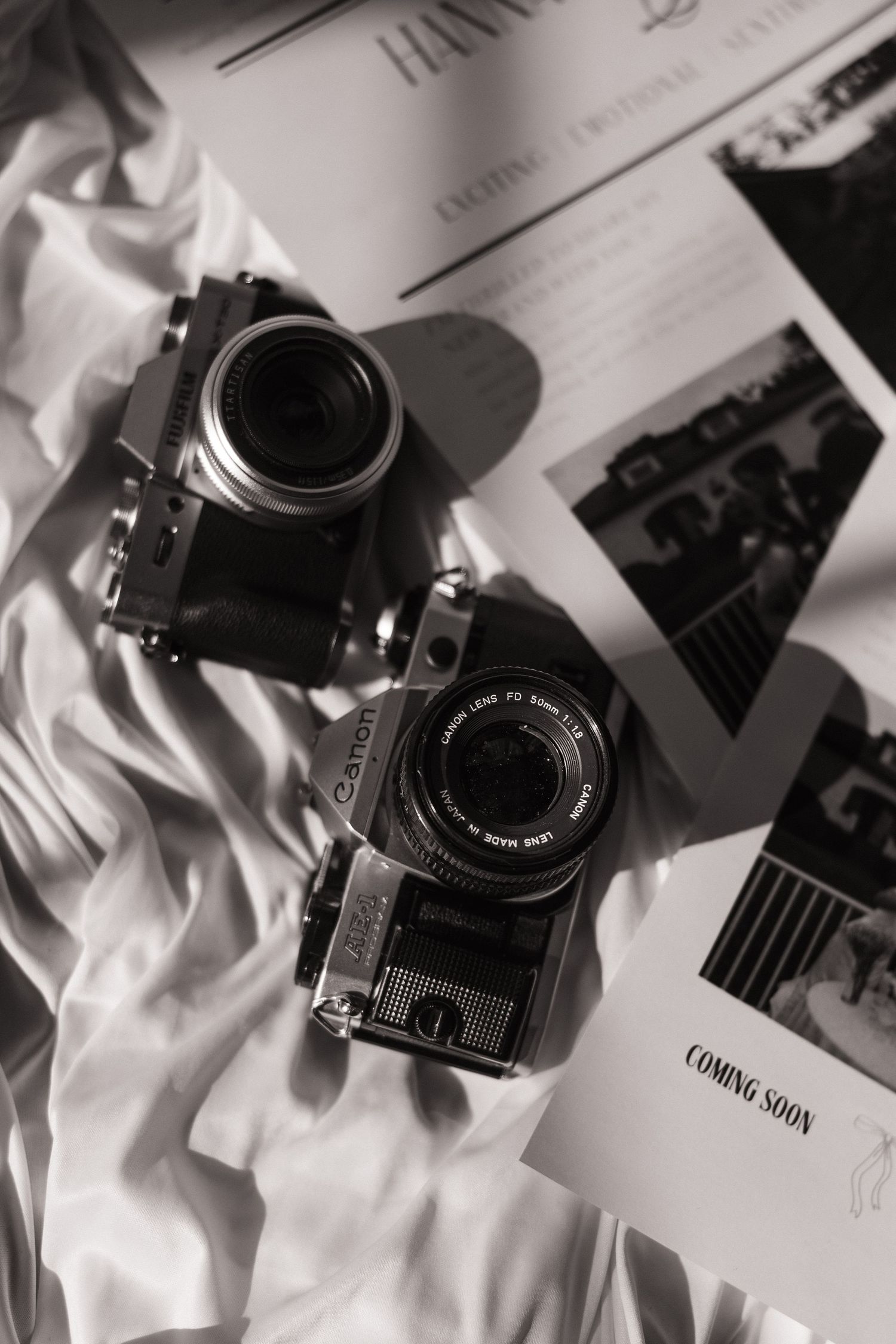 Black and white still life of vintage cameras and photography equipment on white fabric.