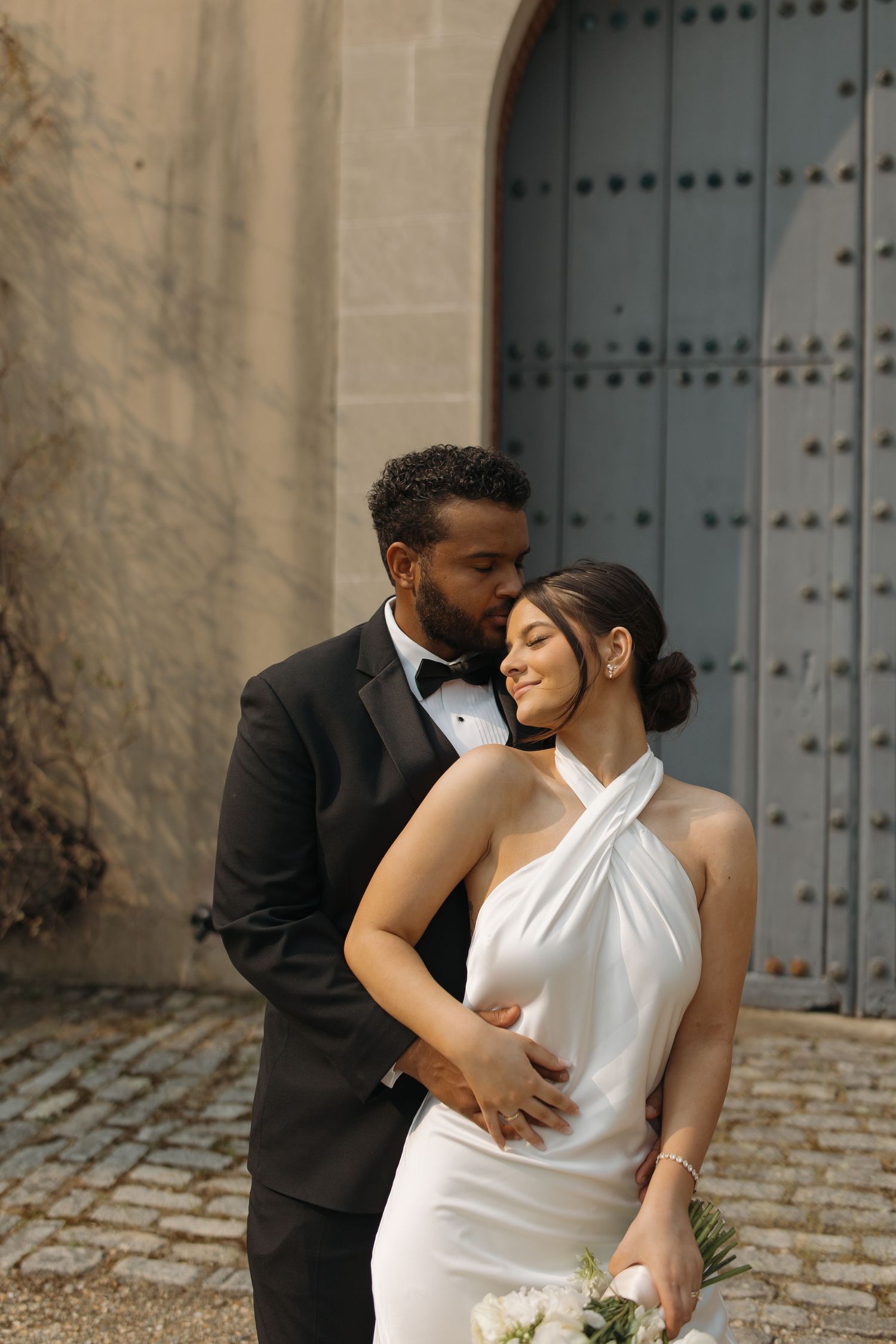 A romantic wedding couple shares an intimate moment on cobblestone streets near a large blue door.