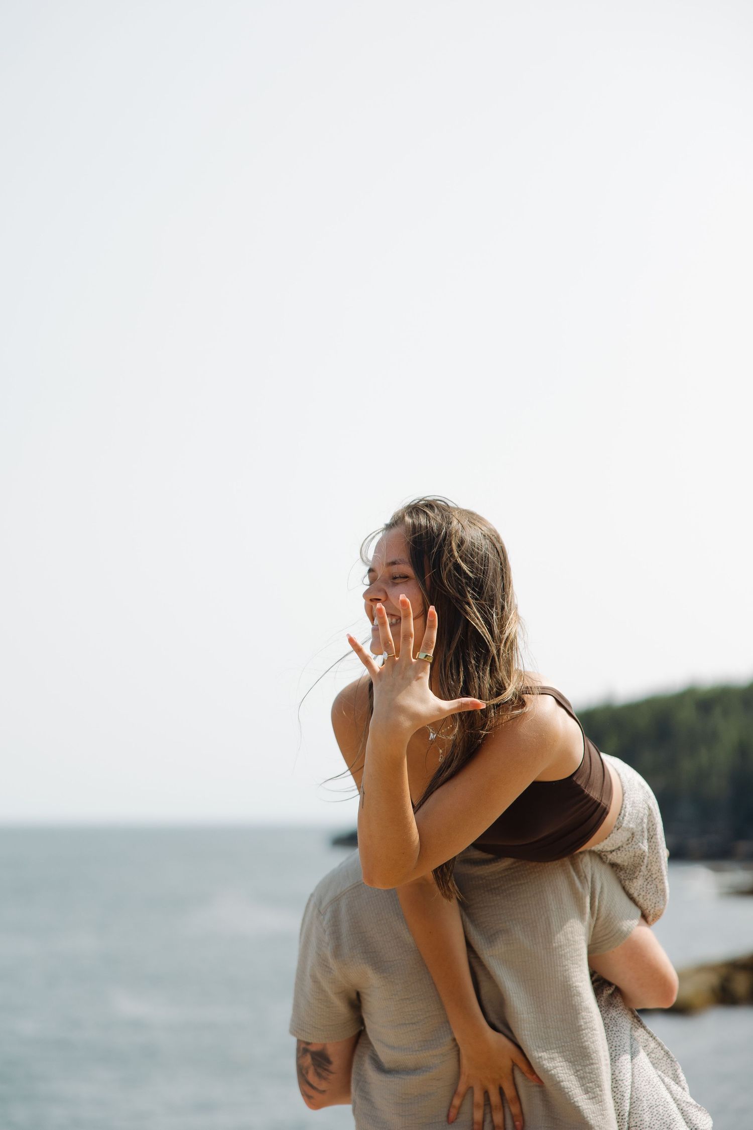 A couple embraces lovingly while looking out at the ocean view from a coastal overlook.
