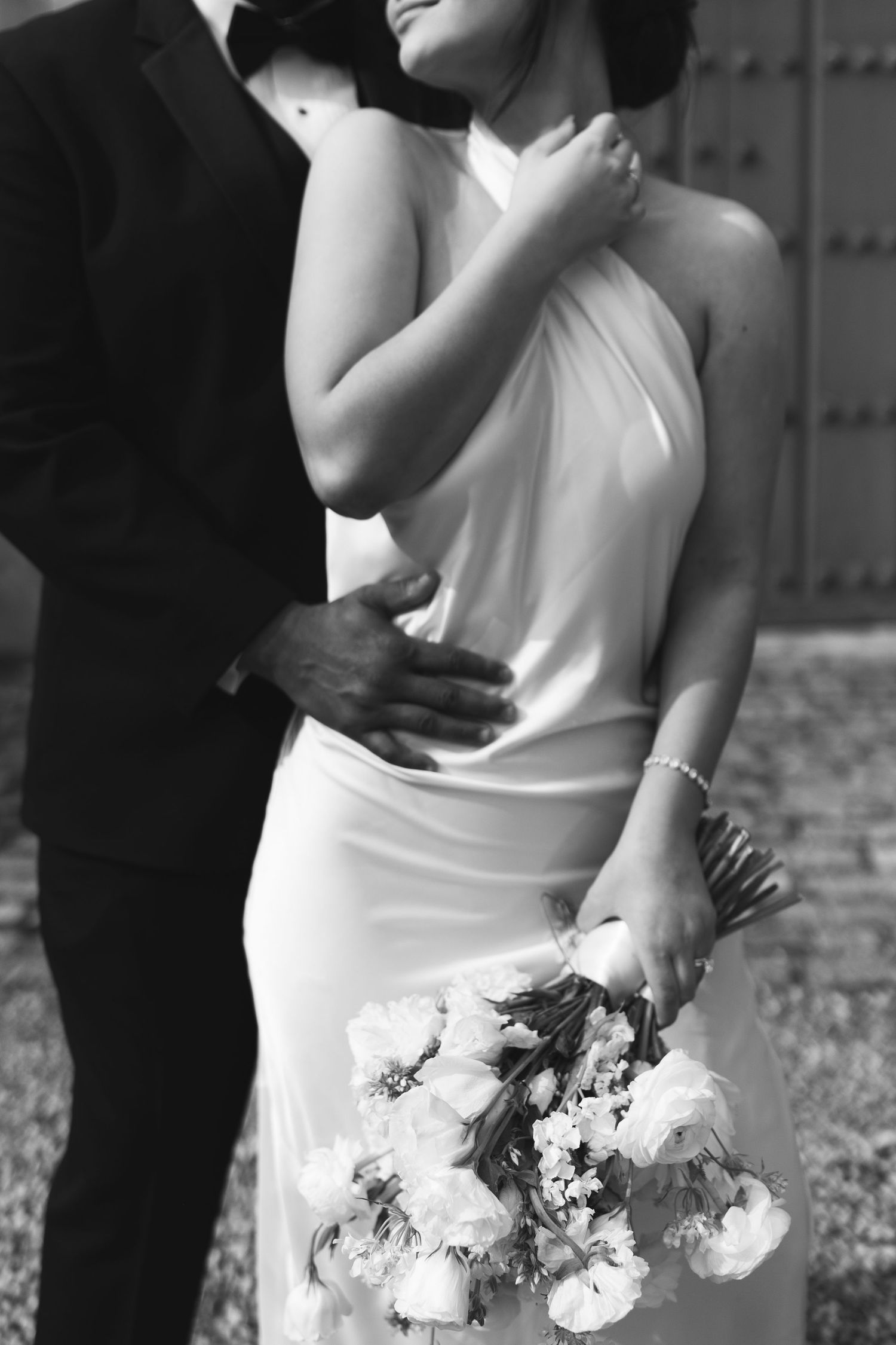Black and white romantic wedding photo series showing couple embracing while bride holds white floral bouquet.