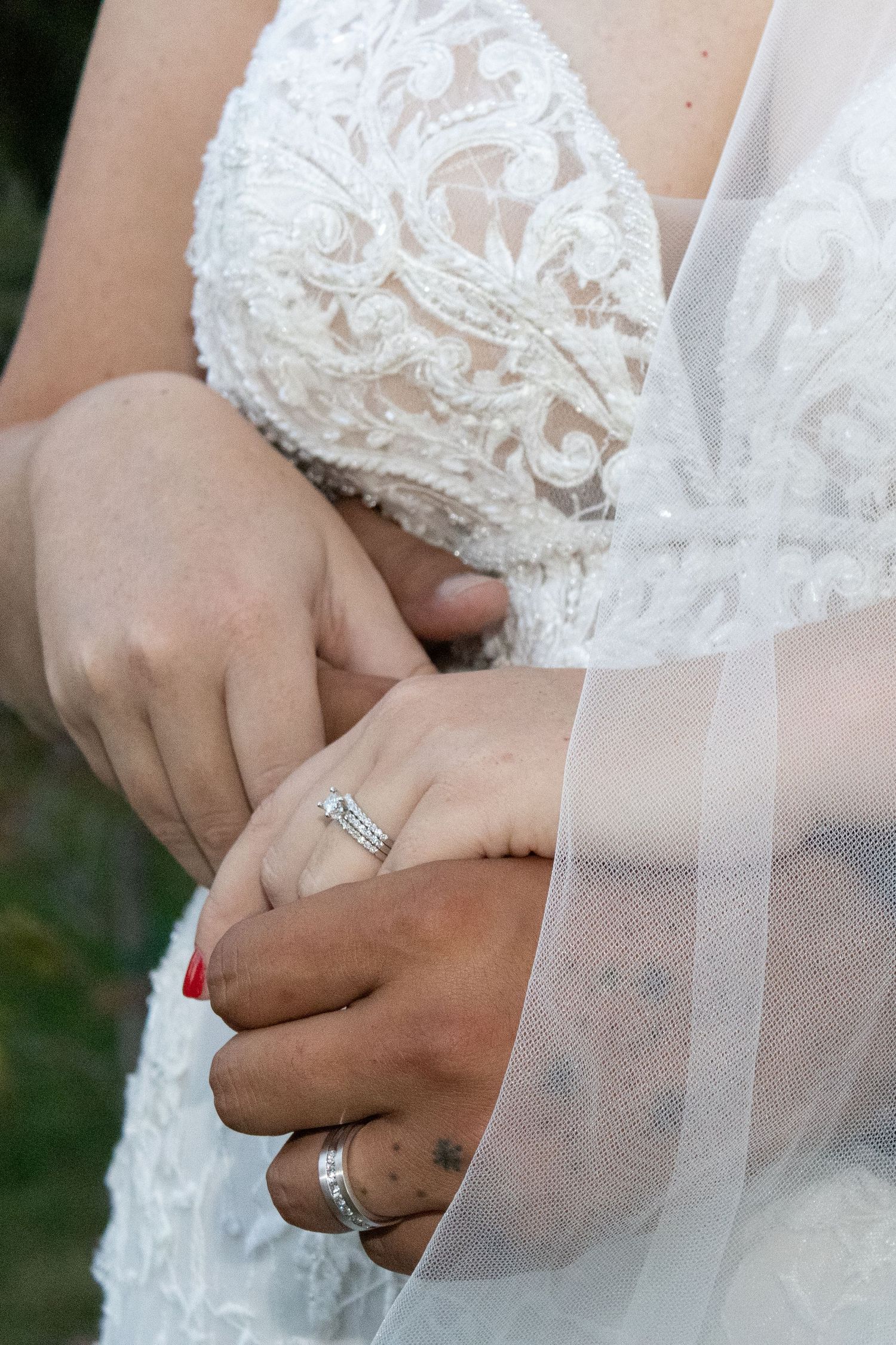 Close-up of delicate white lace wedding dress detail and rings.