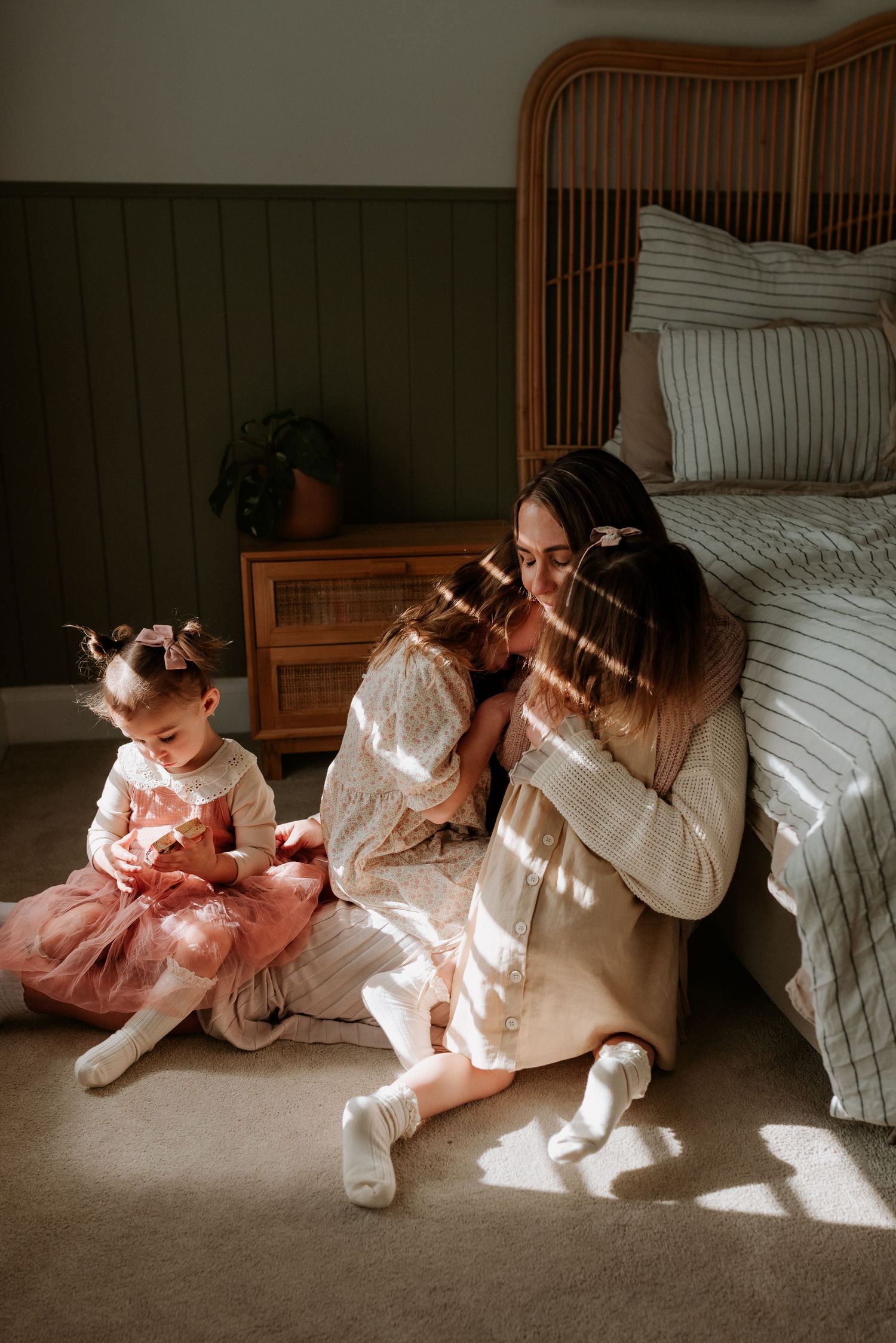 Sunlit indoor family scene with children playing on bedroom floor.