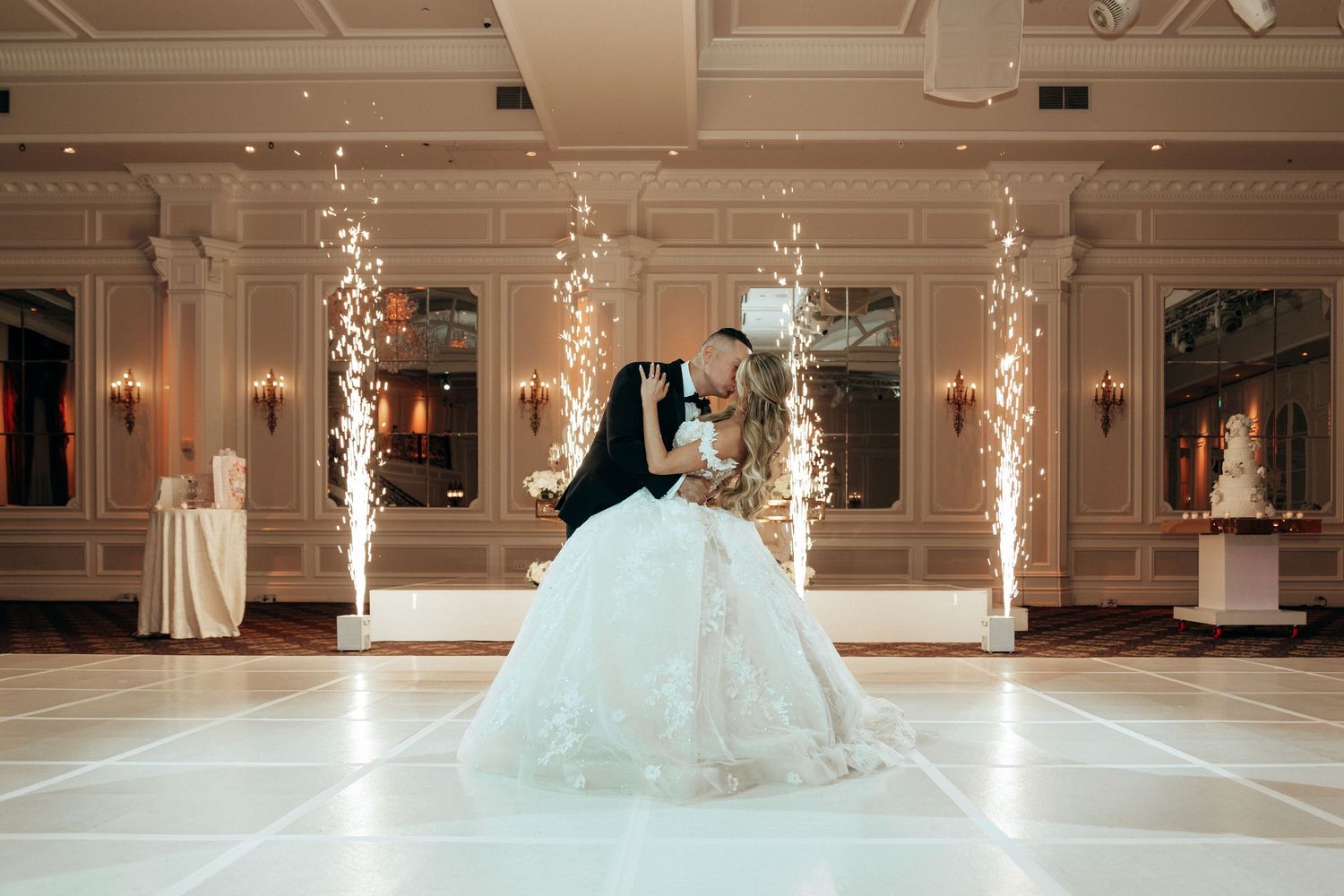 Bride and groom share first dance on white floor with sparkling fireworks and elegant ballroom decor at wedding reception.