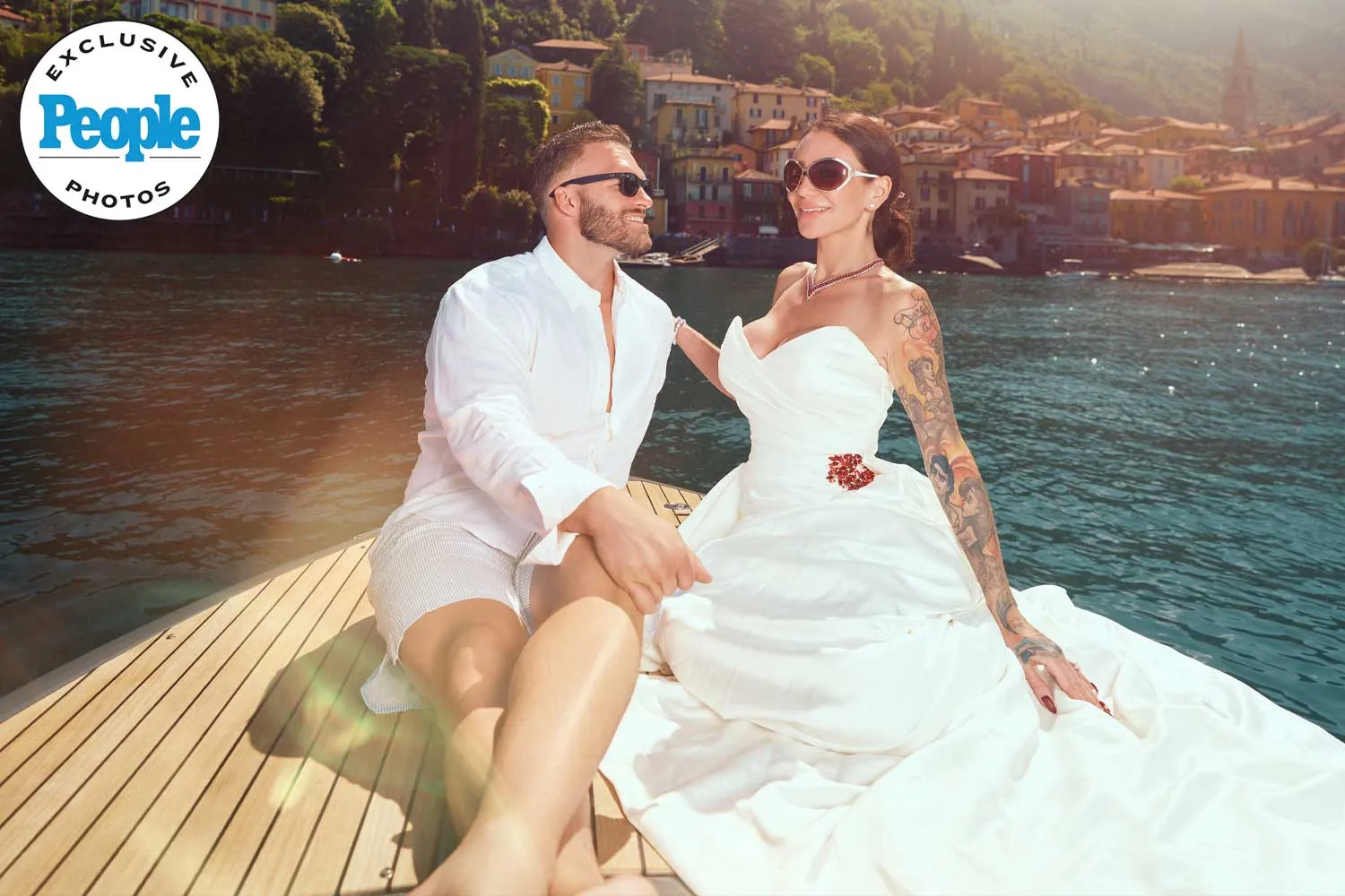 Couple in wedding attire sitting on a boat with scenic waterfront village backdrop, featured in People magazine.
