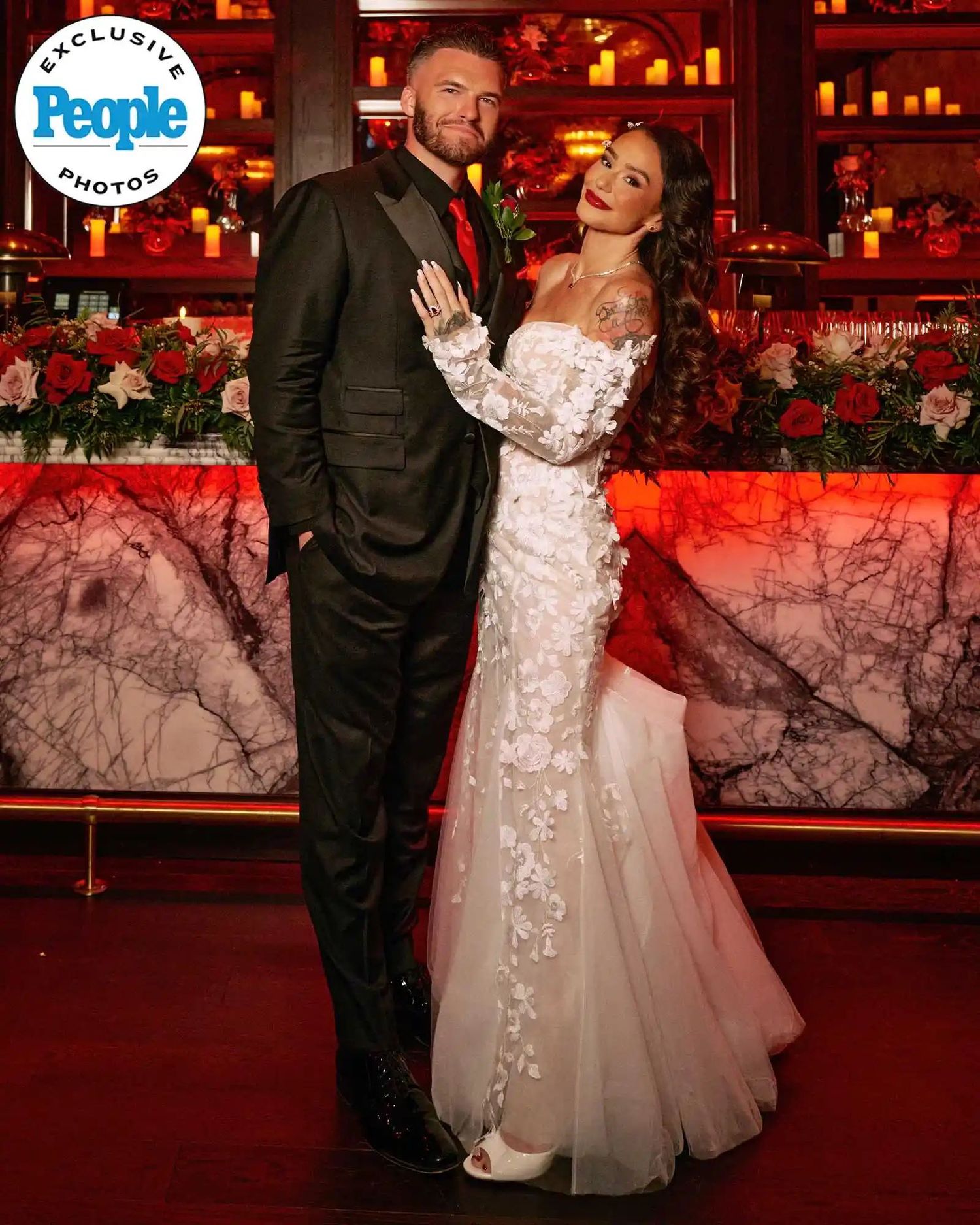 Couple posing in wedding attire, groom in black tuxedo and bride in white floral gown, People magazine exclusive.