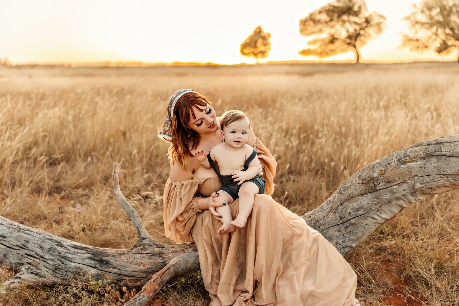 Intimate family moment captured on fallen tree during golden sunset in field.